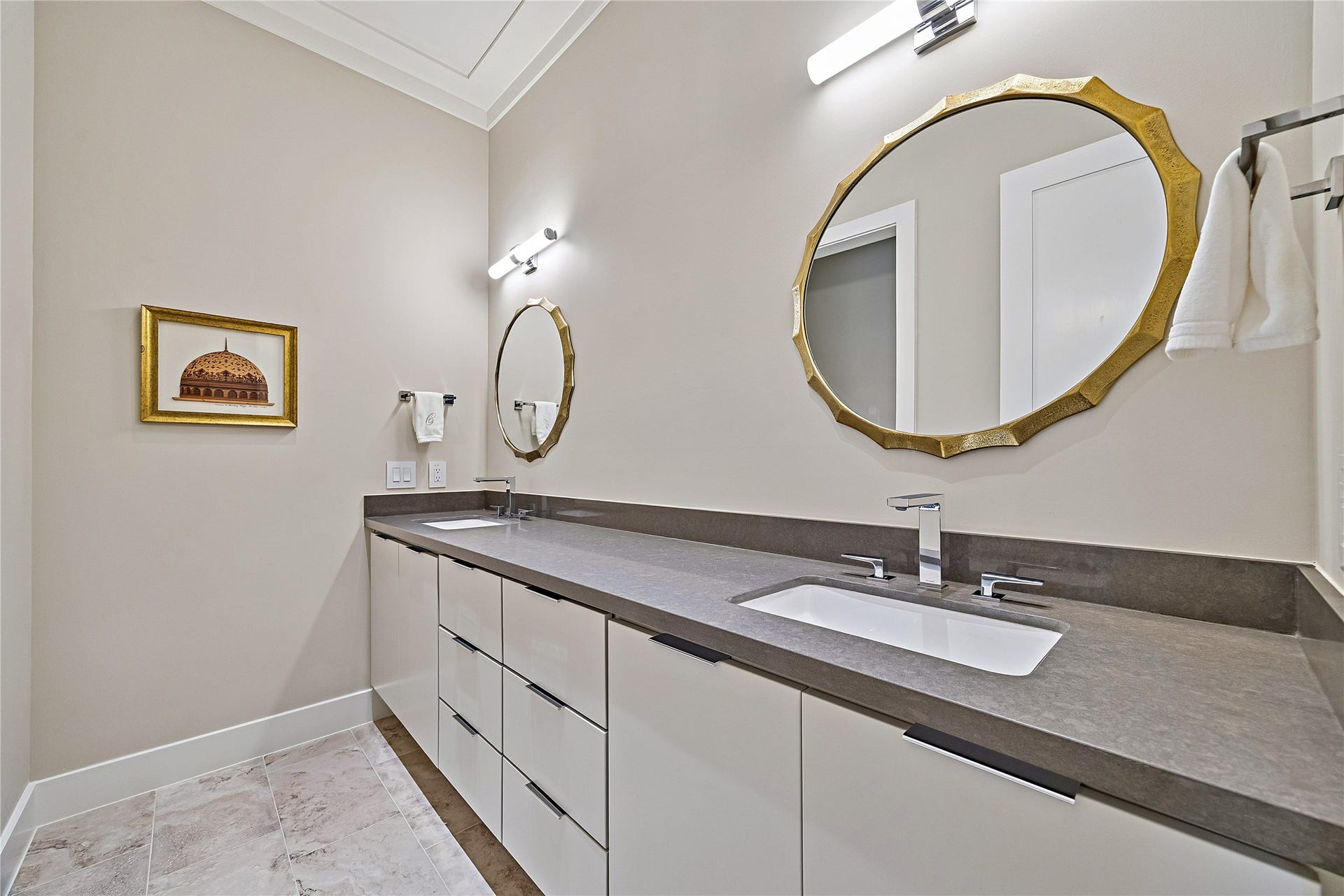 Beautifully appointed bathroom featuring a wide vanity with dual sinks, elegant countertop, decorative mirrors, and refined lighting. Thoughtfully coordinated finishes complement the home's sophisticated interior design.
