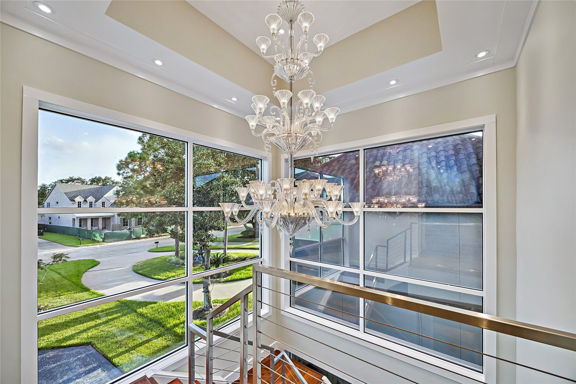 A dramatic architectural perspective showcasing an ornate chandelier suspended beside expansive windows overlooking the lush golf-course landscape. Natural light and elevated views emphasize the connection between the residence and its surroundings.