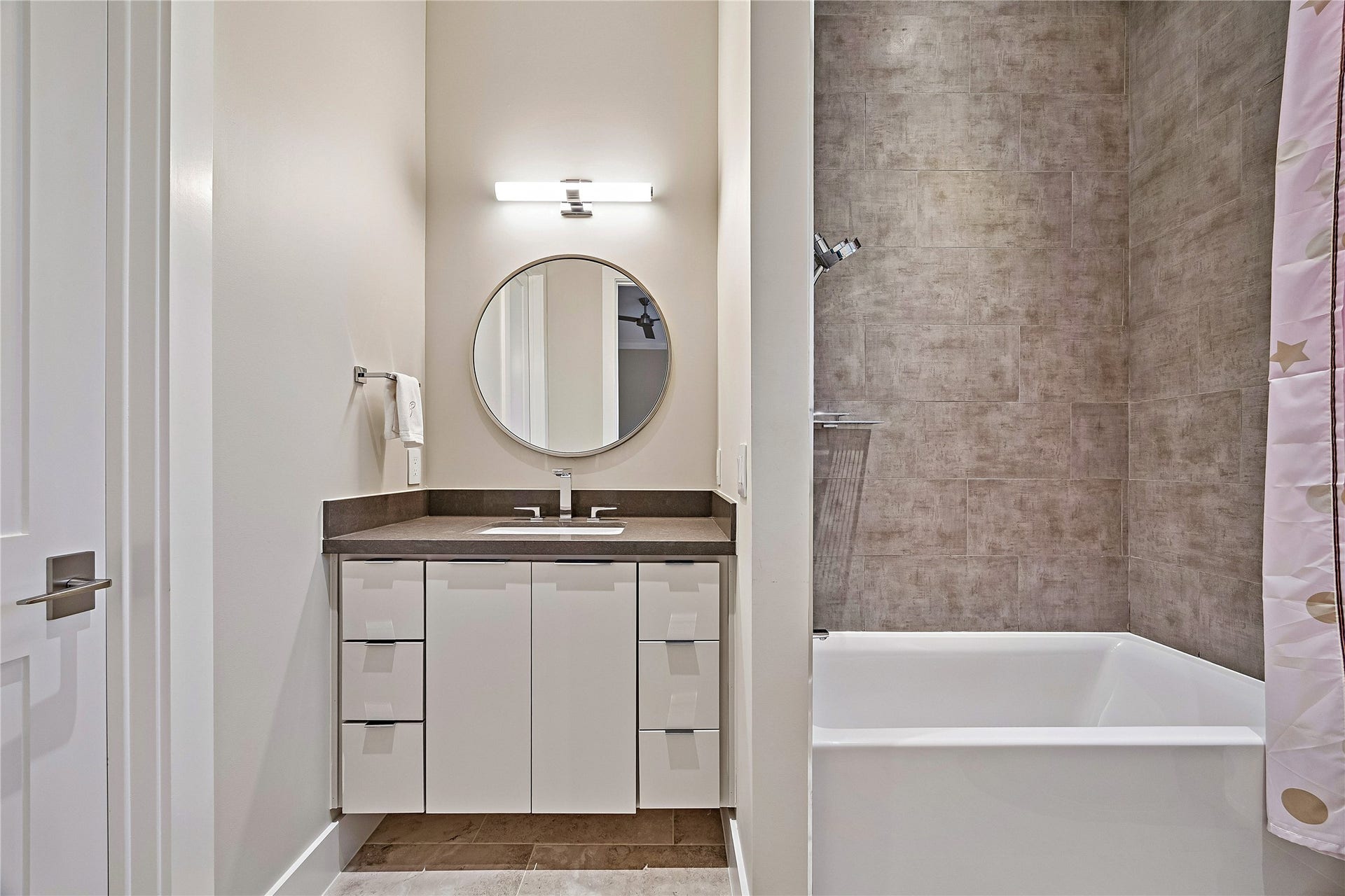 Well-appointed bathroom featuring a contemporary vanity, decorative mirror, and a bathtub and shower combination. Neutral finishes create a clean, sophisticated appearance.
