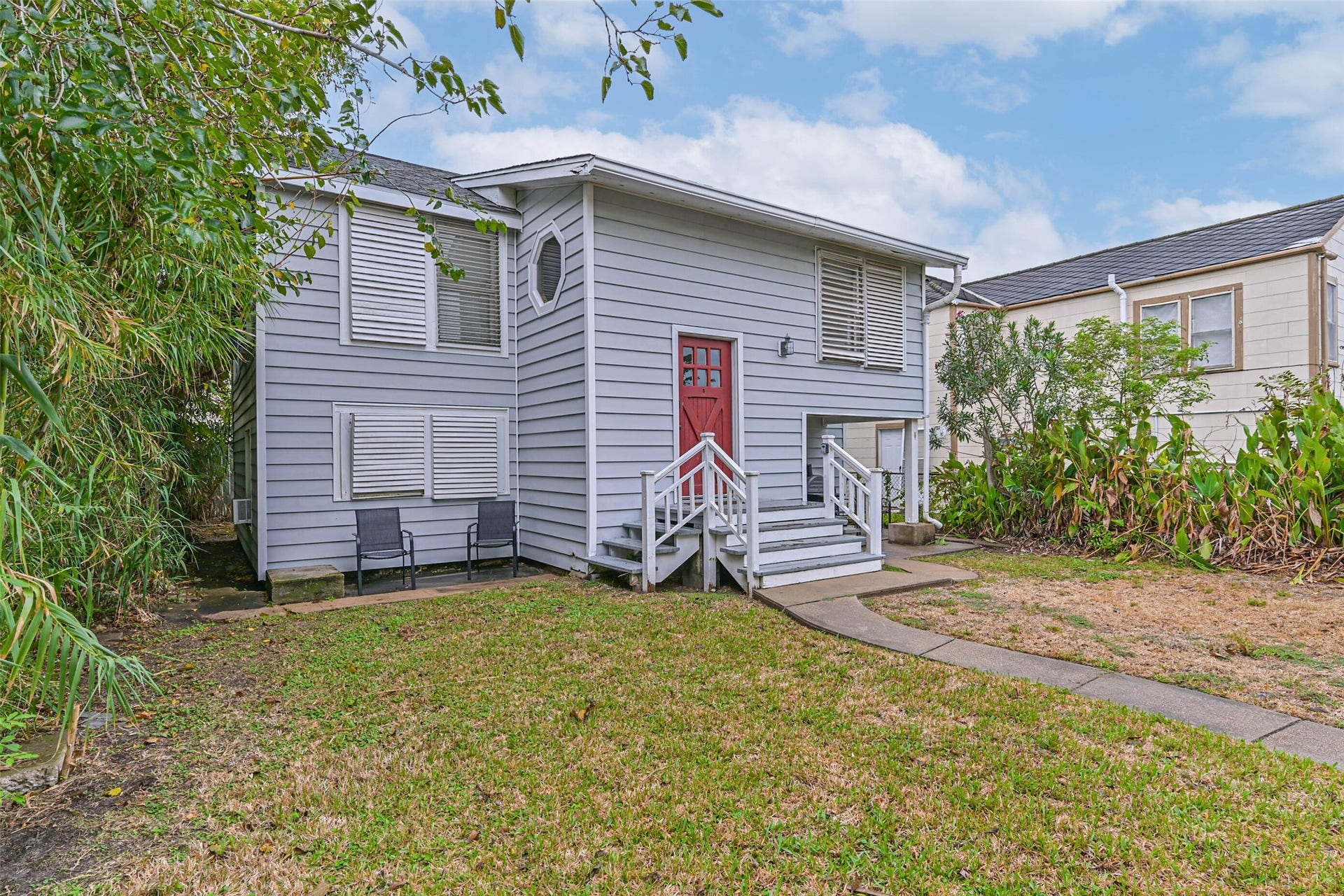 A closer look at the home's exterior, highlighting the distinctive red entry door, raised stairs, and surrounding yard.
