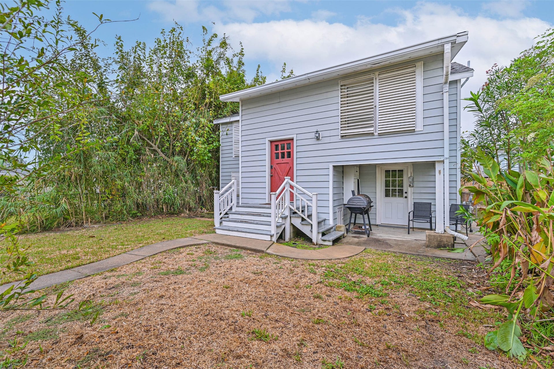 A welcoming exterior view featuring the home's raised entry, red front door, and surrounding greenery.