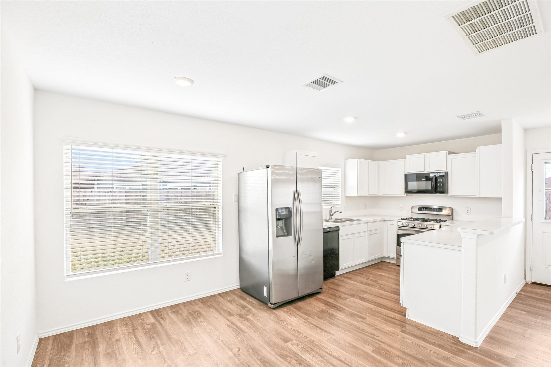 184 Kelly Street, Angleton, TX 77515 Open kitchen and dining area with white cabinetry, stainless appliances, peninsula, window blinds, and wood-look flooring.