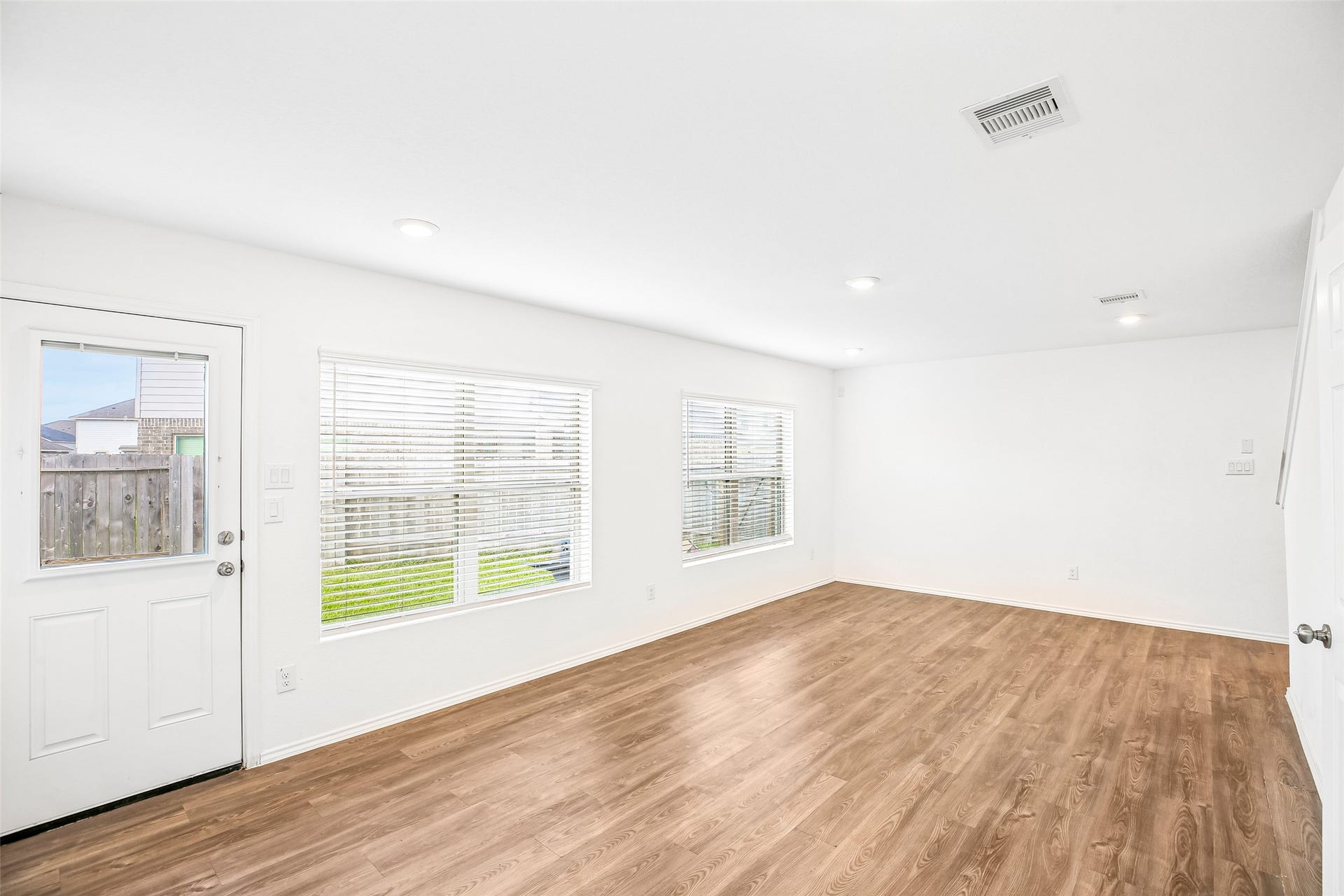 184 Kelly Street, Angleton, TX 77515 Empty living and dining area with multiple window blinds, an entry door, recessed lighting, and wood-look hard flooring.