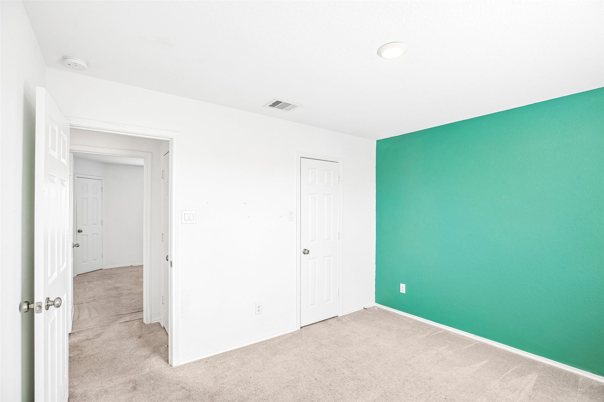 184 Kelly Street, Angleton, TX 77515 Empty carpeted interior room with a vivid teal accent wall, paneled doors, and an open hall doorway.