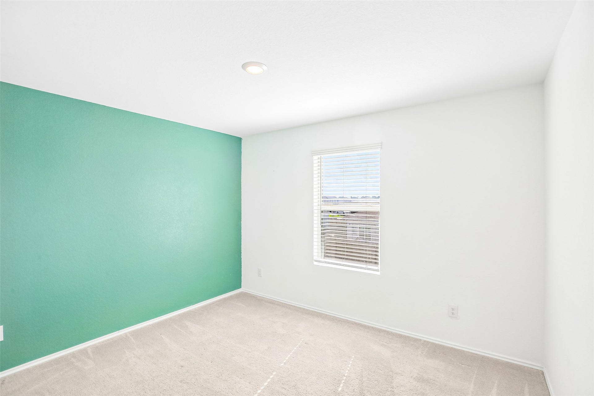 184 Kelly Street, Angleton, TX 77515 Empty carpeted bedroom with a turquoise accent wall, a window with white blinds, and a recessed ceiling light.