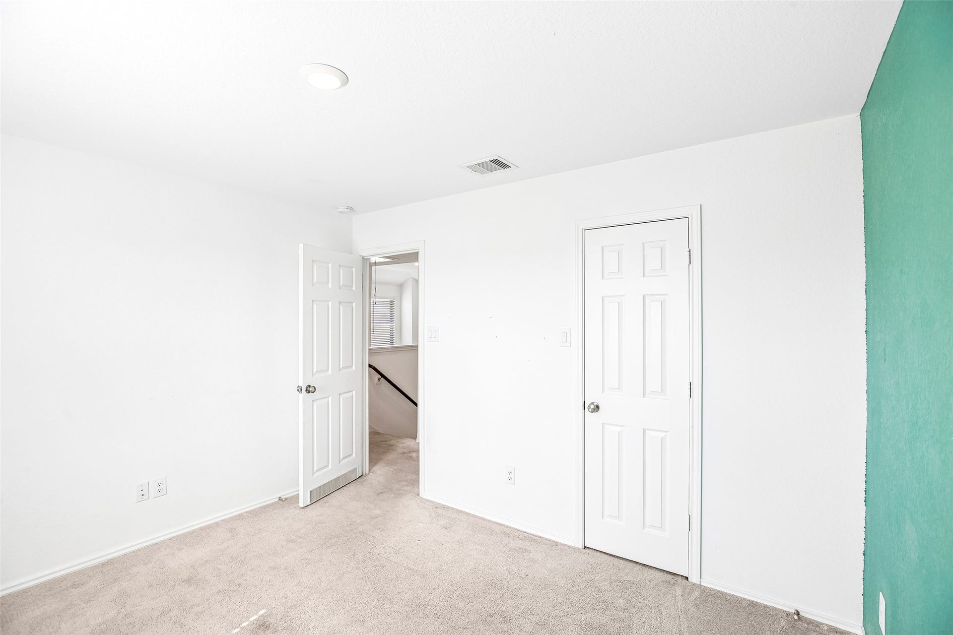 184 Kelly Street, Angleton, TX 77515 Empty carpeted bedroom with an open stairway doorway and a contrasting turquoise wall edge.
