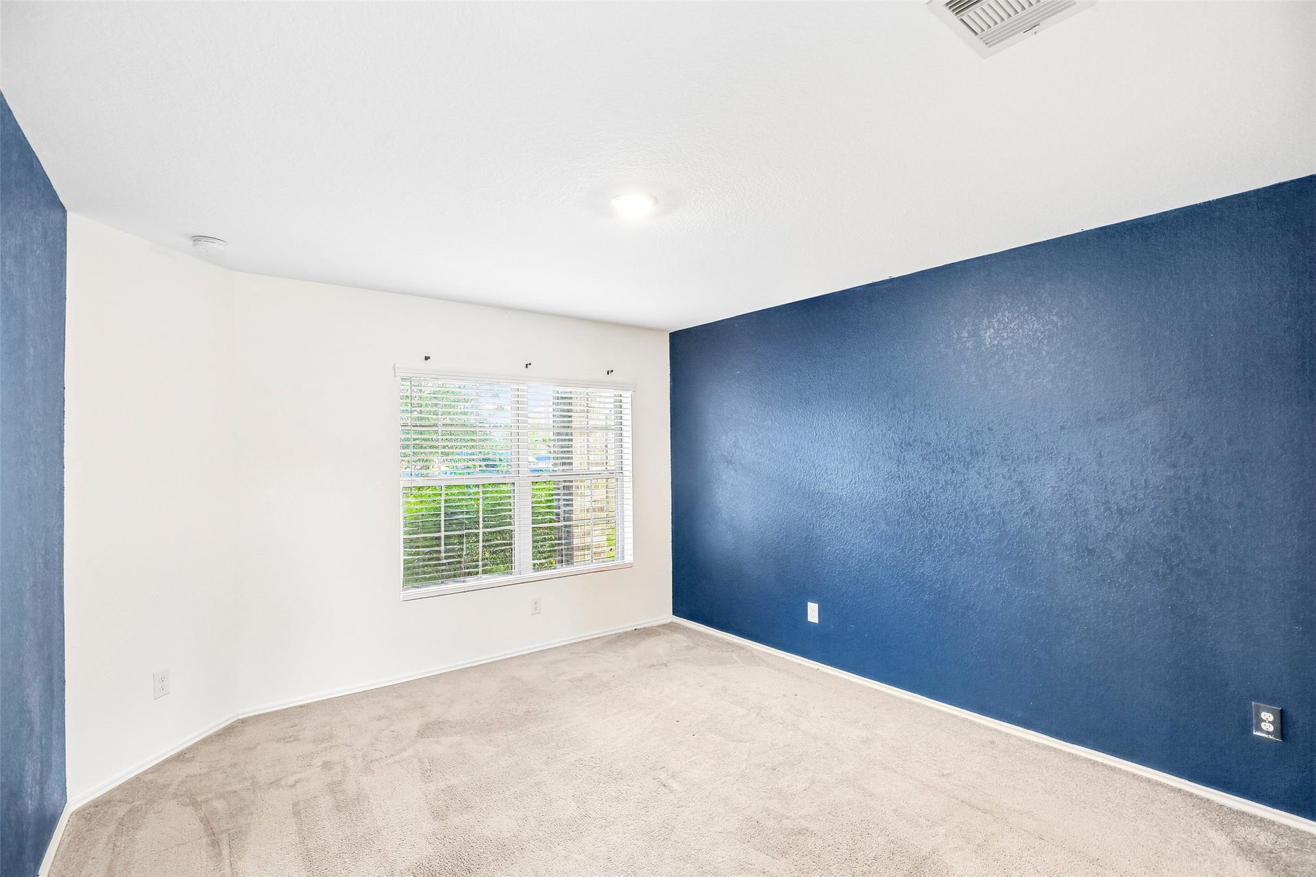 184 Kelly Street, Angleton, TX 77515 Empty carpeted interior room with a window, white blinds, and a blue accent wall.