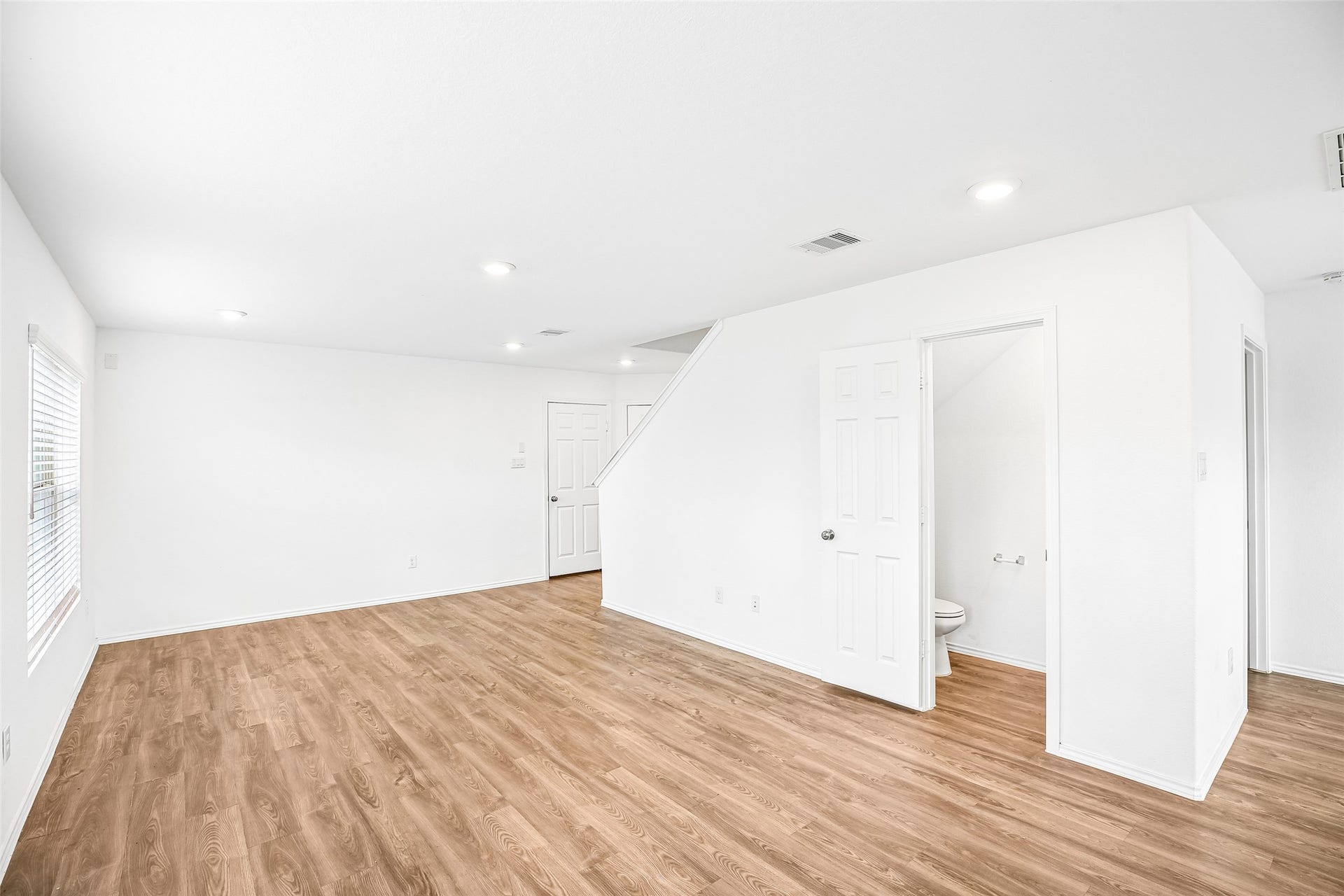 184 Kelly Street, Angleton, TX 77515 Bright, open living and dining area with wood-look flooring, a window with blinds, and a stair opening.