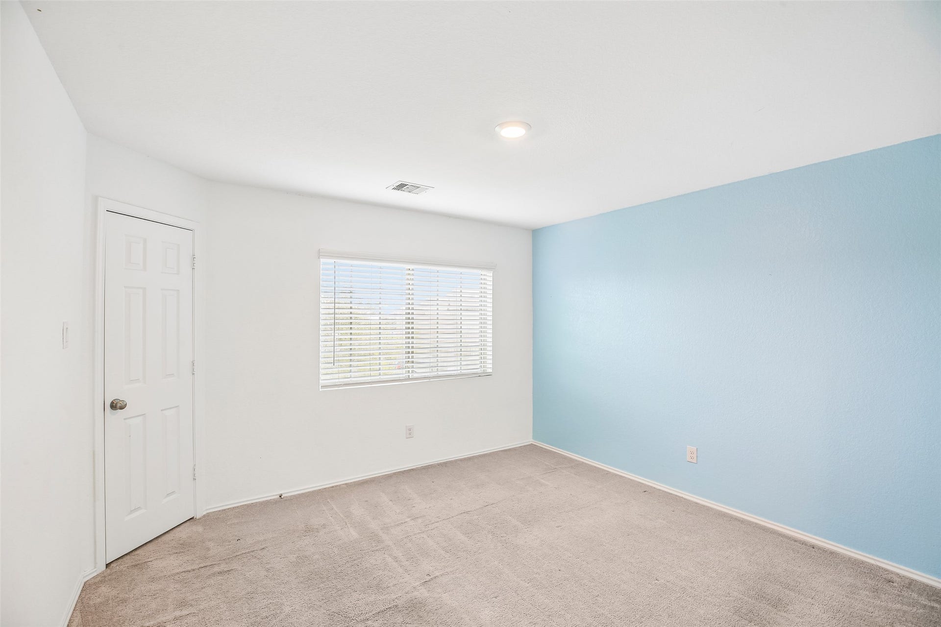 184 Kelly Street, Angleton, TX 77515 Empty carpeted interior room with a window, blinds, white door, and blue accent wall.
