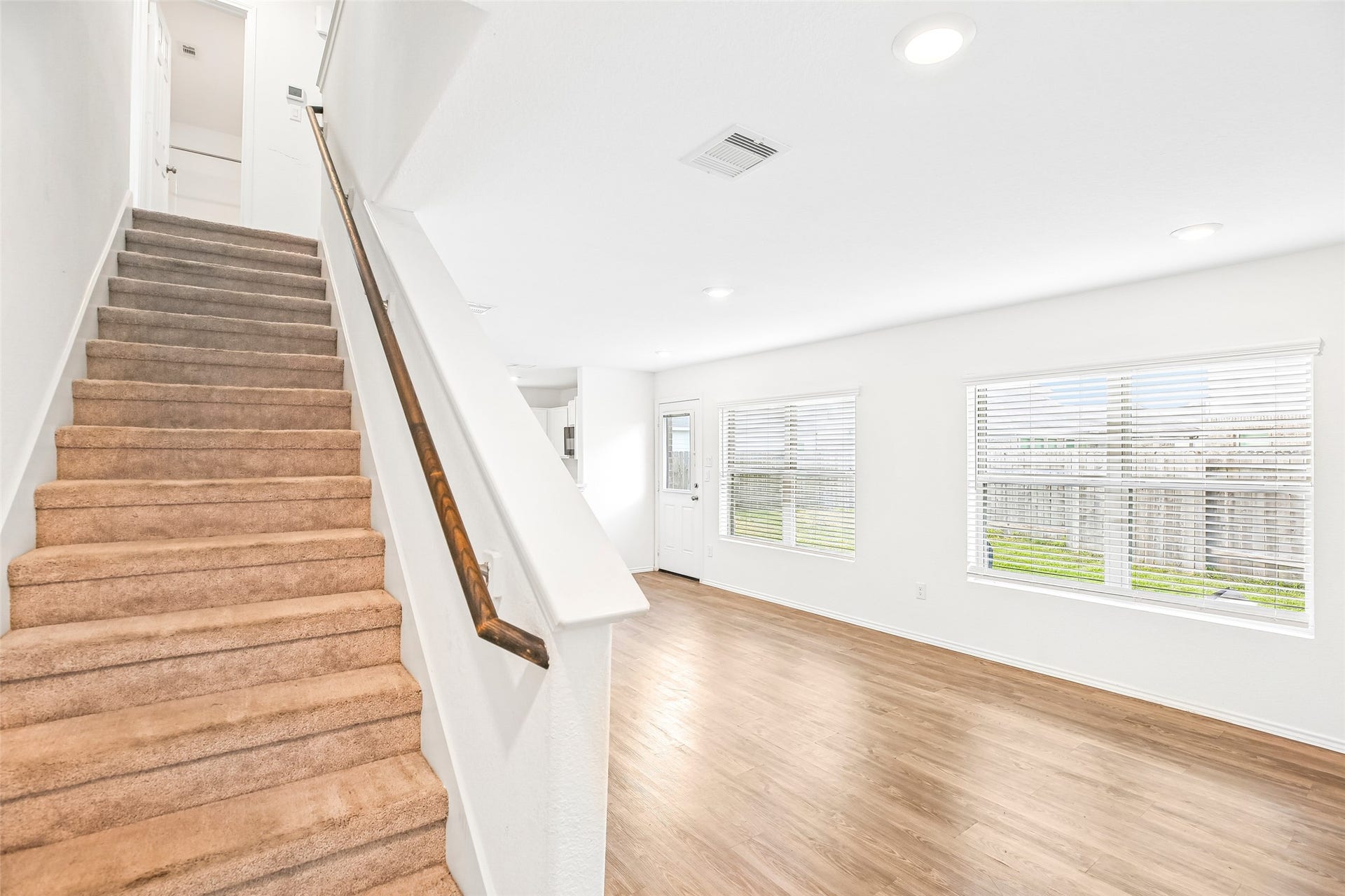 184 Kelly Street, Angleton, TX 77515 Bright, empty living/dining area with a carpeted staircase, wood-look flooring, window blinds, and entry door.