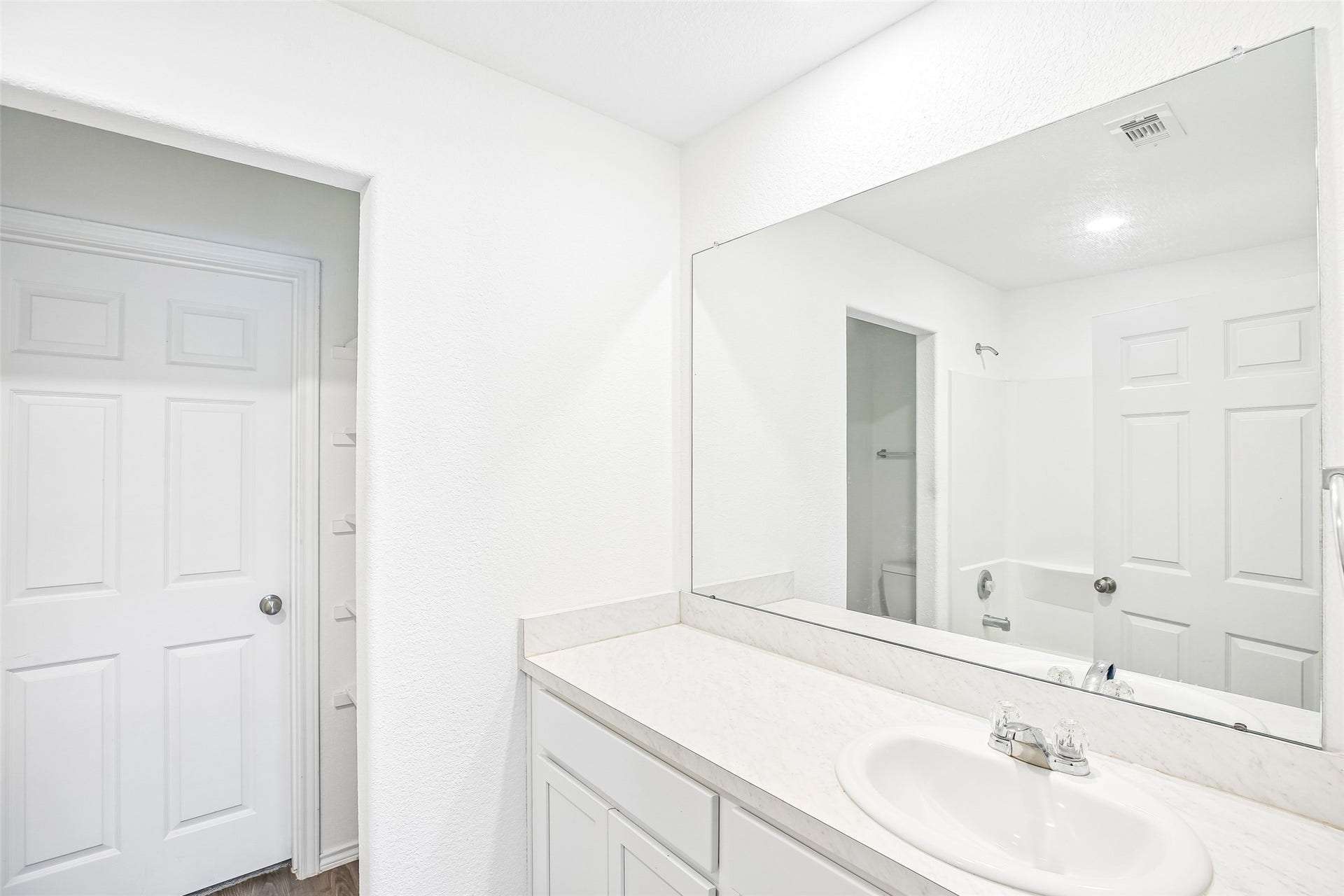 184 Kelly Street, Angleton, TX 77515 Bright bathroom view with a white vanity, large mirror, tub/shower area, white paneled doors, and dark wood-look flooring.