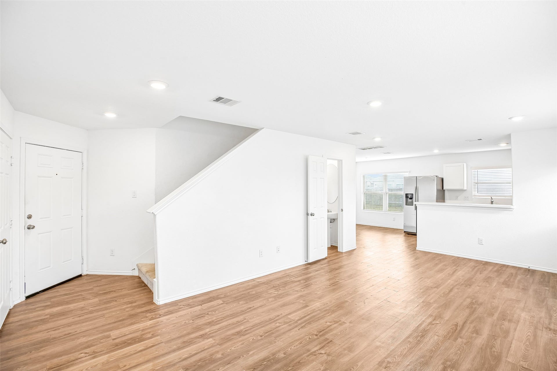 184 Kelly Street, Angleton, TX 77515 Open, empty living and dining area with wood-look flooring, stairs, and a connected kitchen view.