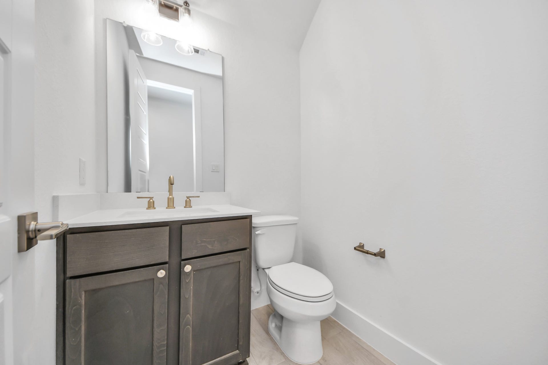 Sophisticated half bathroom adorned with contemporary finishes. The elegant 5-panel door welcomes you to a space where style meets functionality. Notice the sleek hardware accents that add a touch of modern charm. The vanity boasts light-colored countertops, beautifully complemented by a tasteful vanity light, creating a well-lit and inviting atmosphere.