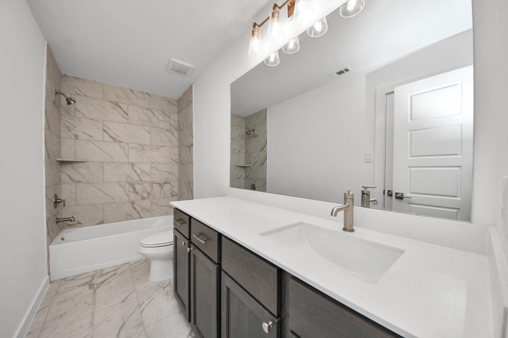 Secondary bath features tile flooring, bath/shower combo with tile surround, light stained wood cabinets, beautiful light countertop.