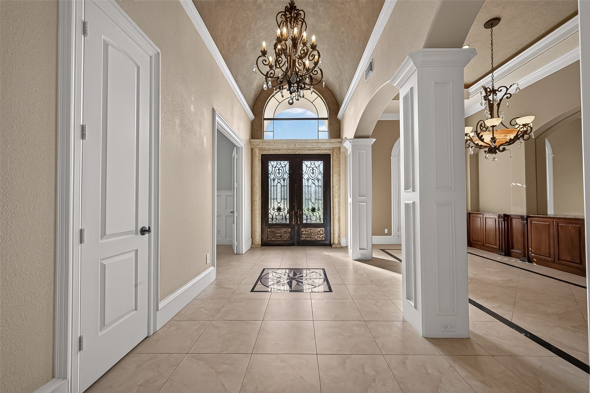 4011 Westerdale Drive, Fulshear, TX 77441 The grand foyer sets the tone for this luxurious home, showcasing dramatic iron French doors, a soaring arched ceiling, soft cove lighting, a statement chandelier, and custom decorative accent tile that immediately makes a lasting impression.