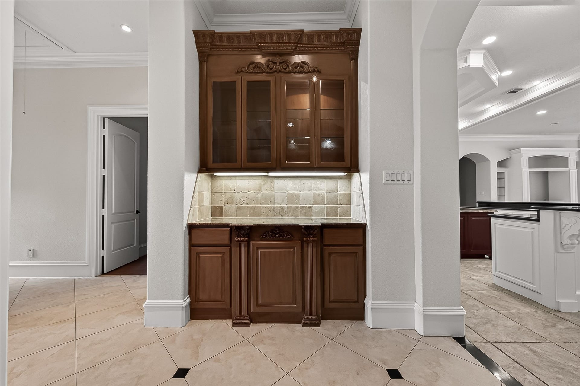 4011 Westerdale Drive, Fulshear, TX 77441 Adjacent to the formal living and dining rooms, the custom dry bar is both a functional amenity and a decorative showpiece. Rich, built-in cabinetry showcases ornate carved detailing, illuminated glass-front doors, and a natural stone backsplash accented by under-cabinet lighting. Designed to complement the homes refined aesthetic, this inviting space is ideal for effortless entertaining and elegant display.