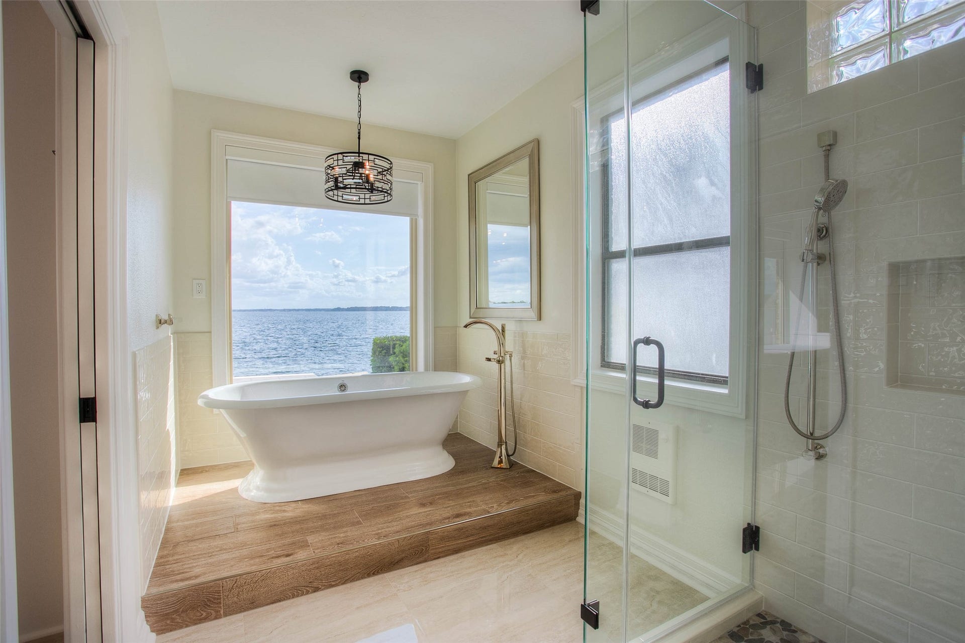 12092 Sagittarius Drive E, Willis, TX 77318 Luxurious bathroom featuring a freestanding tub with stunning open water views, complemented by a modern glass-enclosed shower and elegant fixtures.