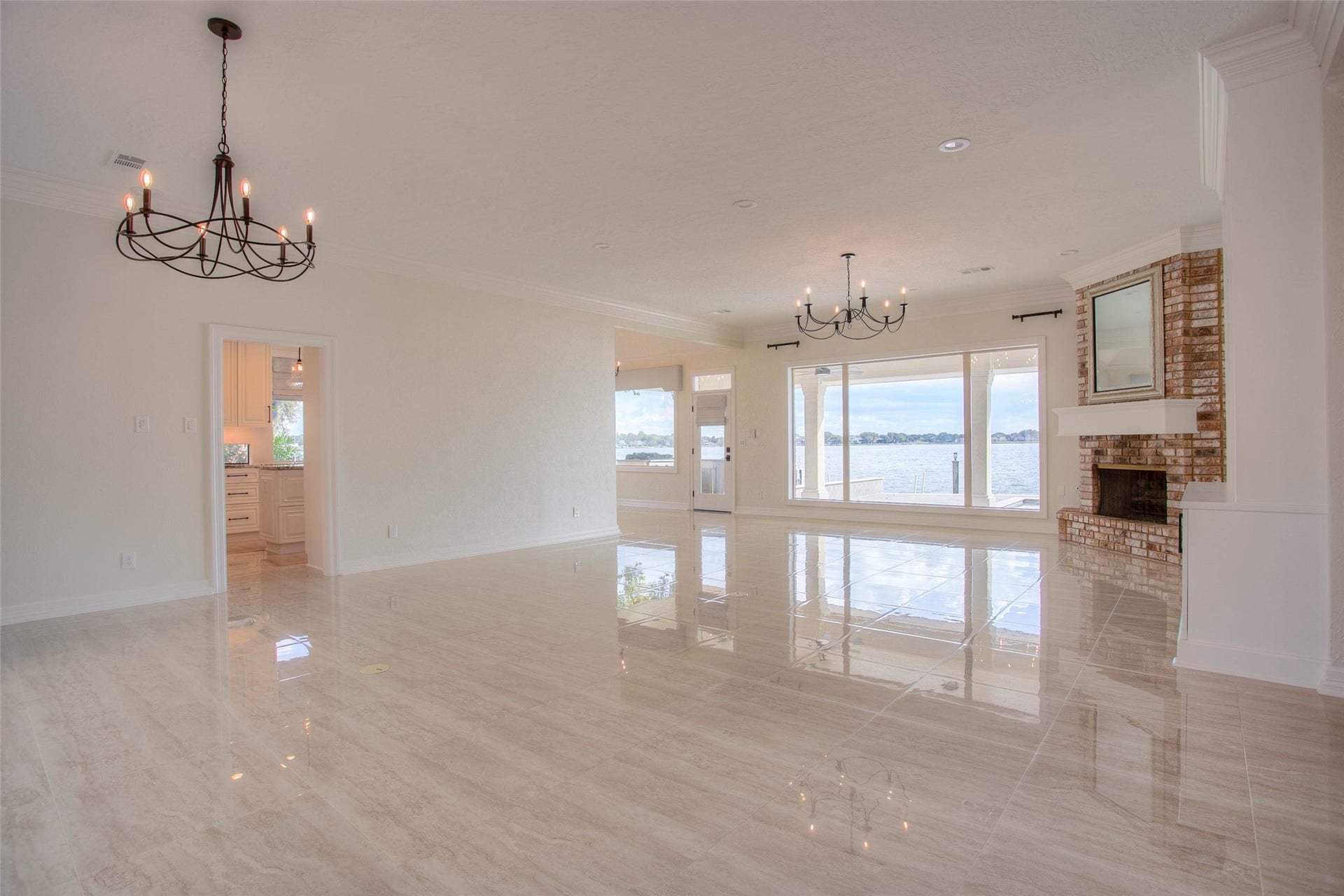 12092 Sagittarius Drive E, Willis, TX 77318 Expansive living area with elegant chandeliers, a cozy brick fireplace, and stunning waterfront views through large windows.