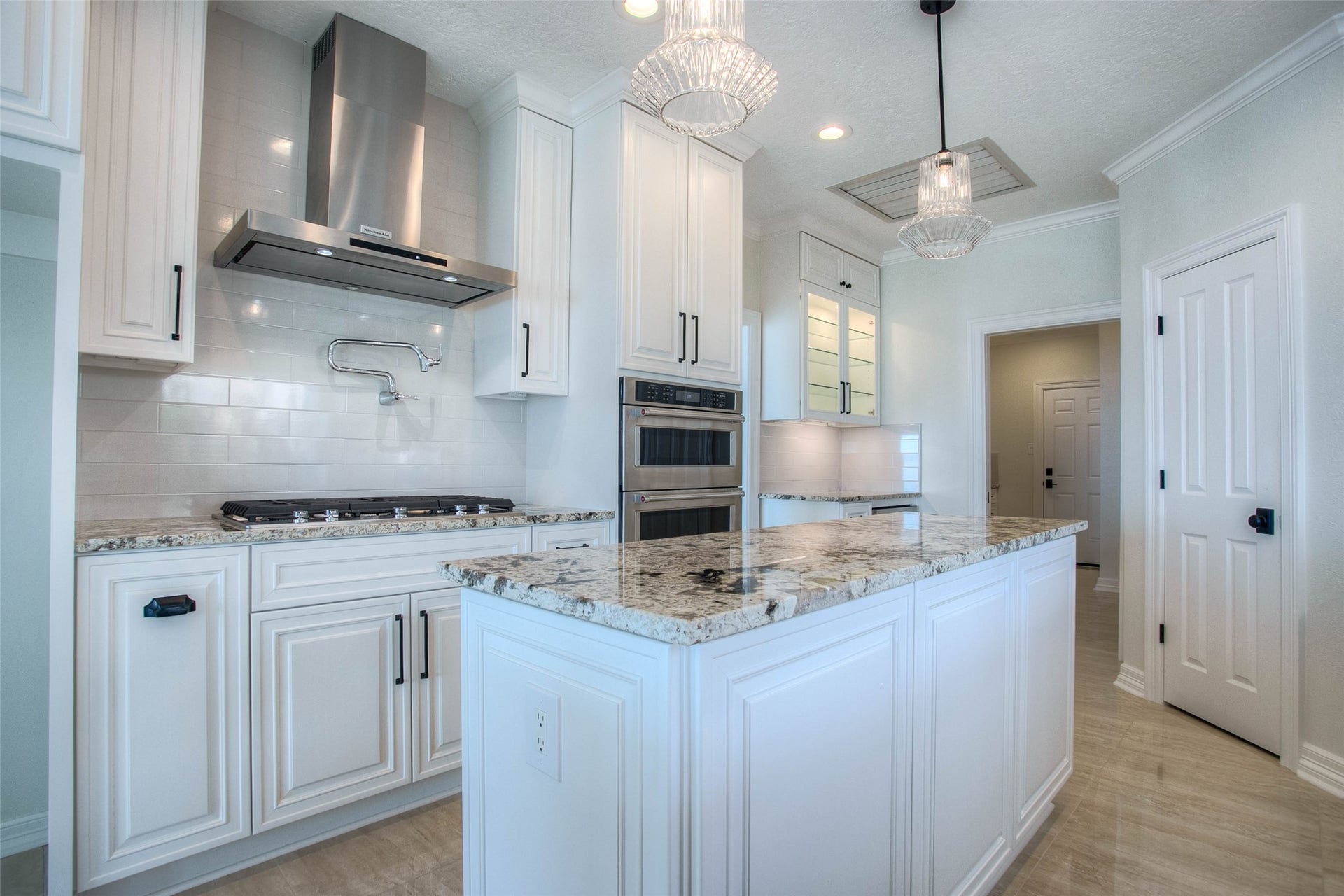 12092 Sagittarius Drive E, Willis, TX 77318 Elegant kitchen featuring a spacious island with granite countertops, modern stainless steel appliances, and custom white cabinetry, all enhanced by stylish pendant lighting.