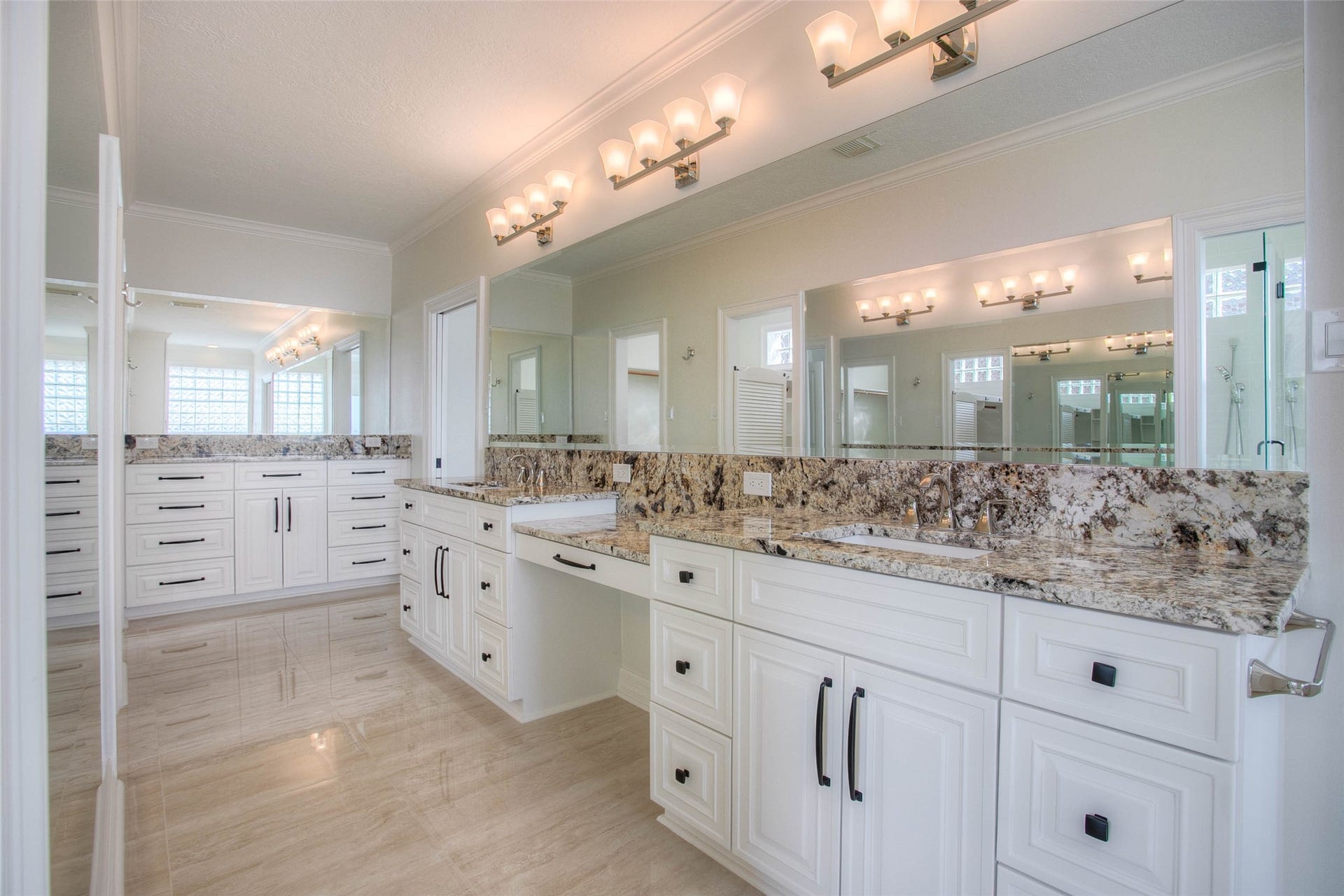 12092 Sagittarius Drive E, Willis, TX 77318 Luxurious bathroom featuring dual granite-topped vanities, elegant lighting, and ample storage with sleek white cabinetry.