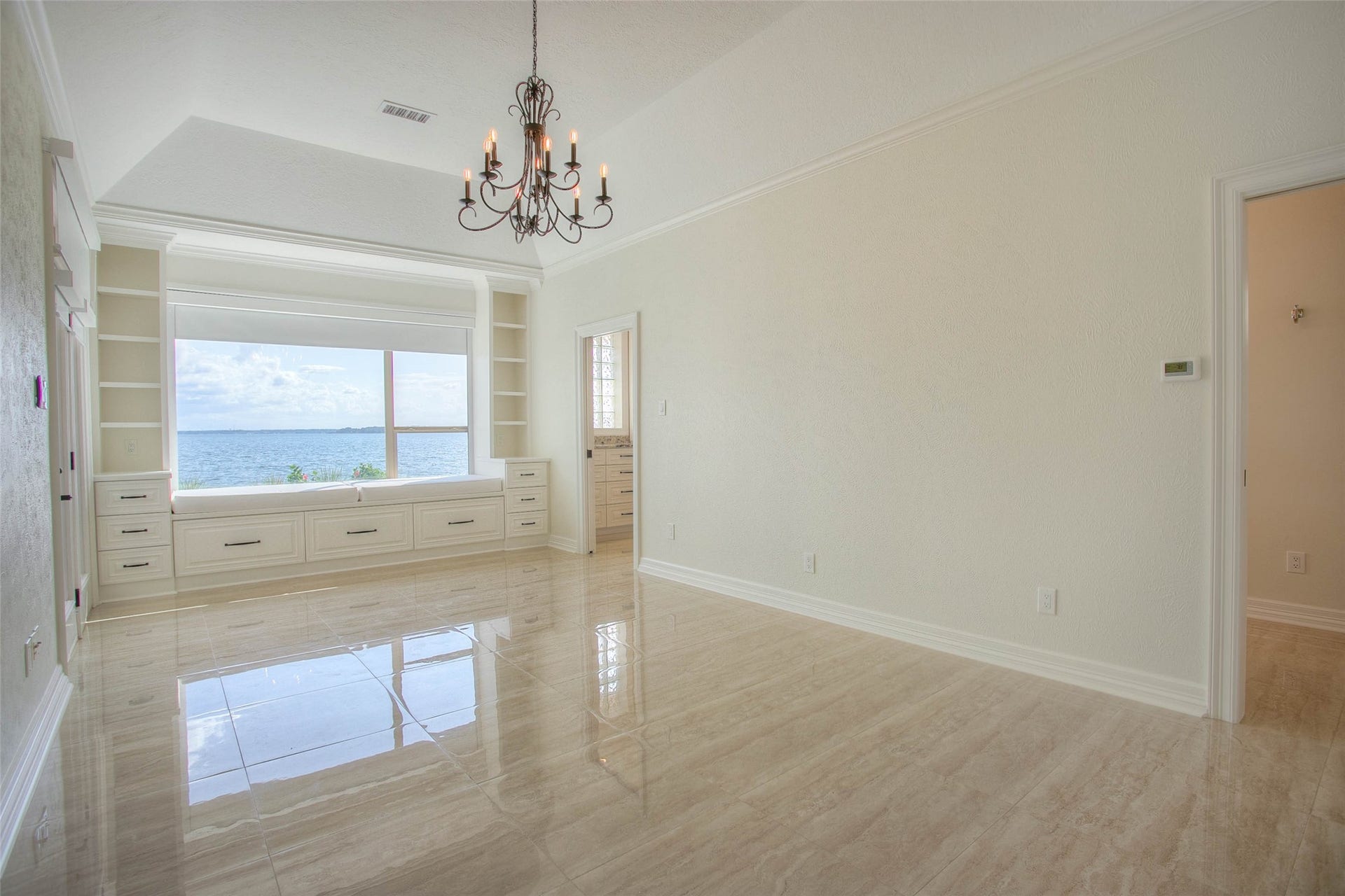 12092 Sagittarius Drive E, Willis, TX 77318 Bright primary bedroom with stunning water views, elegant chandelier, and built-in storage under a large window seat.