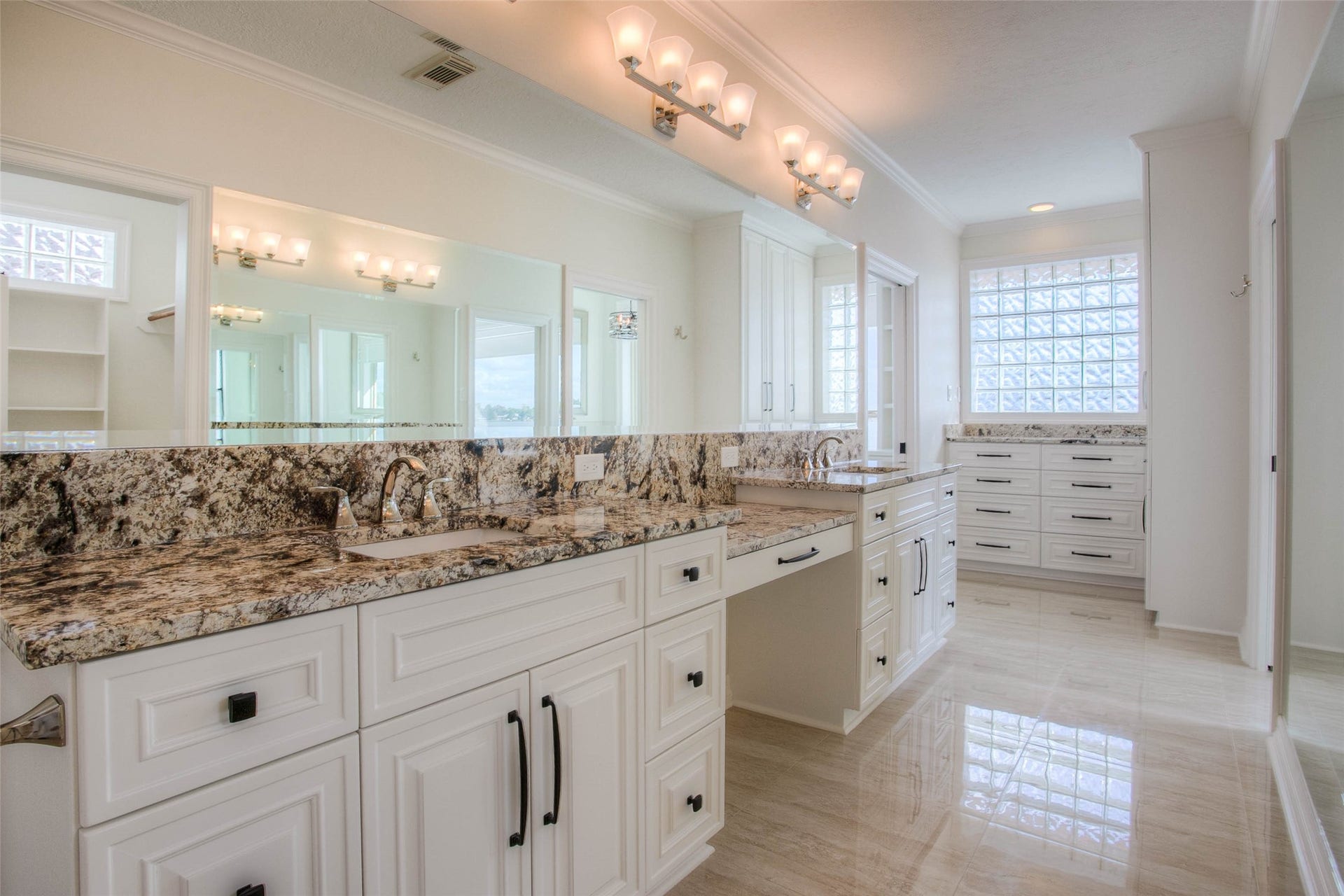 12092 Sagittarius Drive E, Willis, TX 77318 Luxurious bathroom featuring dual vanities with elegant granite countertops, ample storage, and stylish lighting, all enhanced by natural light through glass block windows.