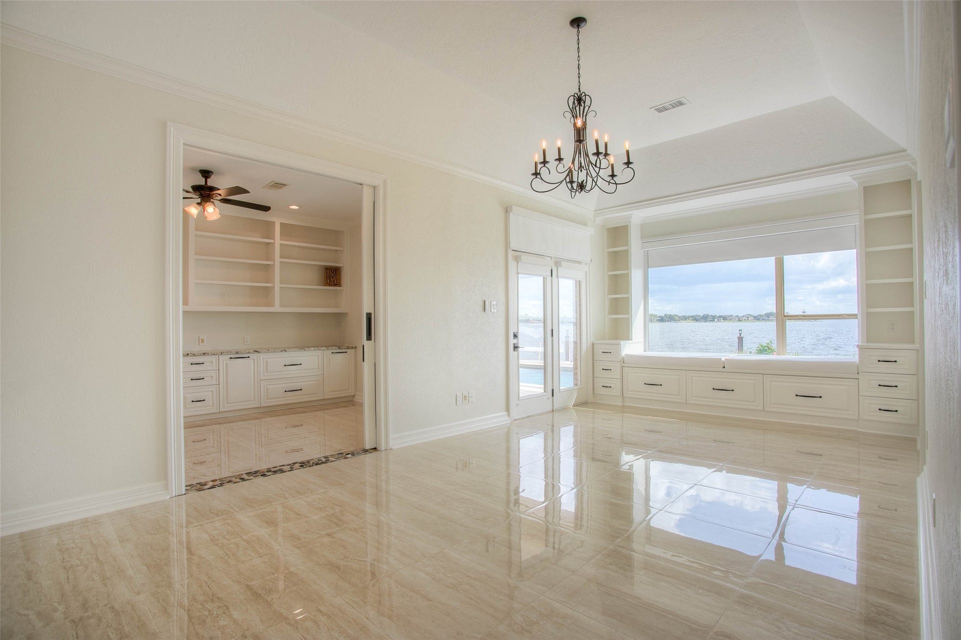 12092 Sagittarius Drive E, Willis, TX 77318 Elegant waterfront view from primary bedroom with gleaming tile floors, a stylish chandelier, and large windows offering Built-in shelving and seating and ample storage, while glass doors lead to an inviting outdoor space.