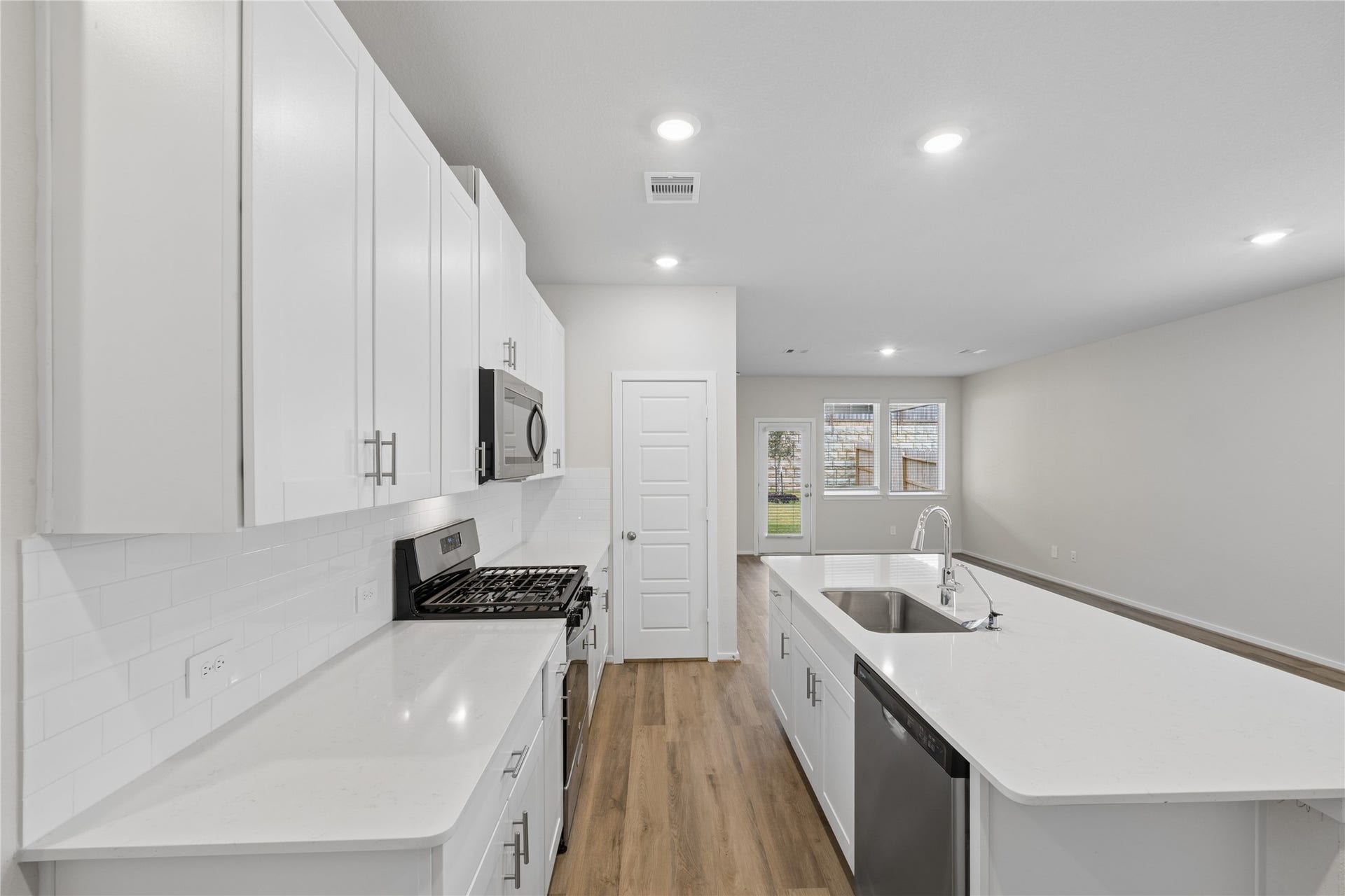 384 Sunrise Ranch Dr, Montgomery, TX 77316 Modern kitchen featuring sleek white cabinetry, stainless steel appliances, and a spacious island with a sink, seamlessly leading into an open living area.