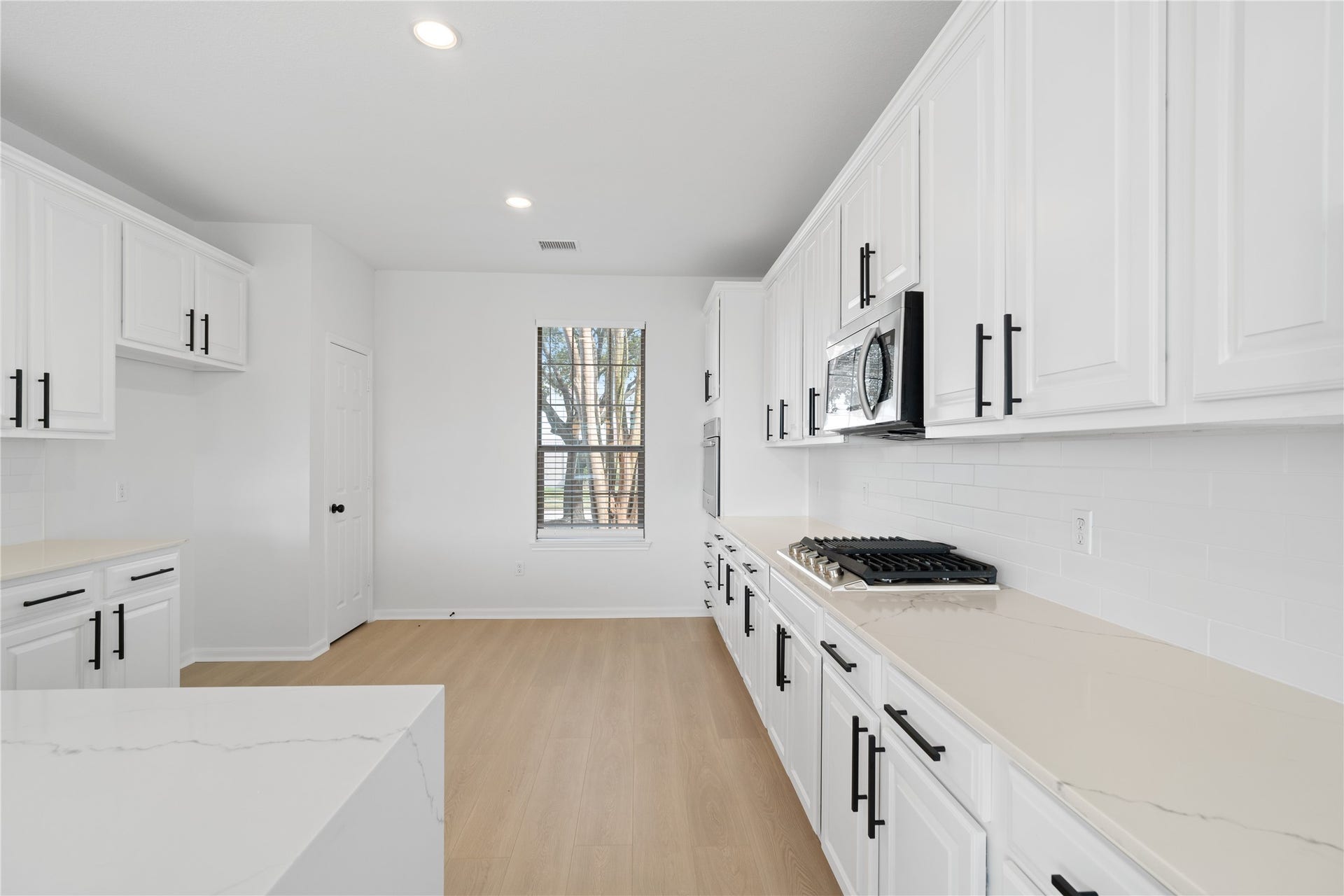 21611 Manitou Falls Lane, Katy, TX 77449 Kitchen Bright kitchen offers extensive white cabinetry with contrasting black hardware, stone-look countertops, subway-style tile backsplash, recessed lighting, and generous workspace.