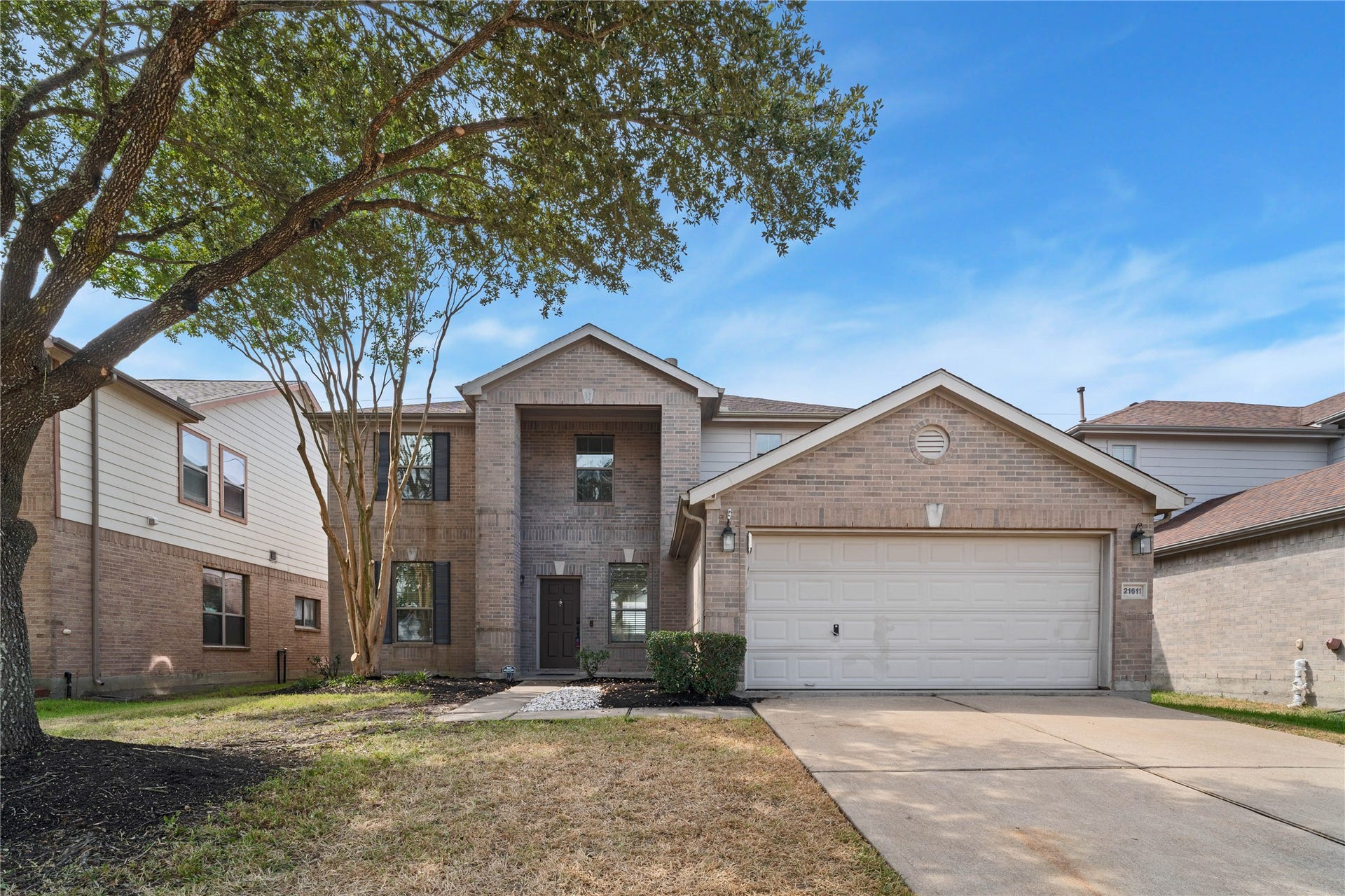 21611 Manitou Falls Lane, Katy, TX 77449 Front Exterior Two-story brick exterior features an attached garage, covered entry, mature shade trees, and a walkway leading to the front door.