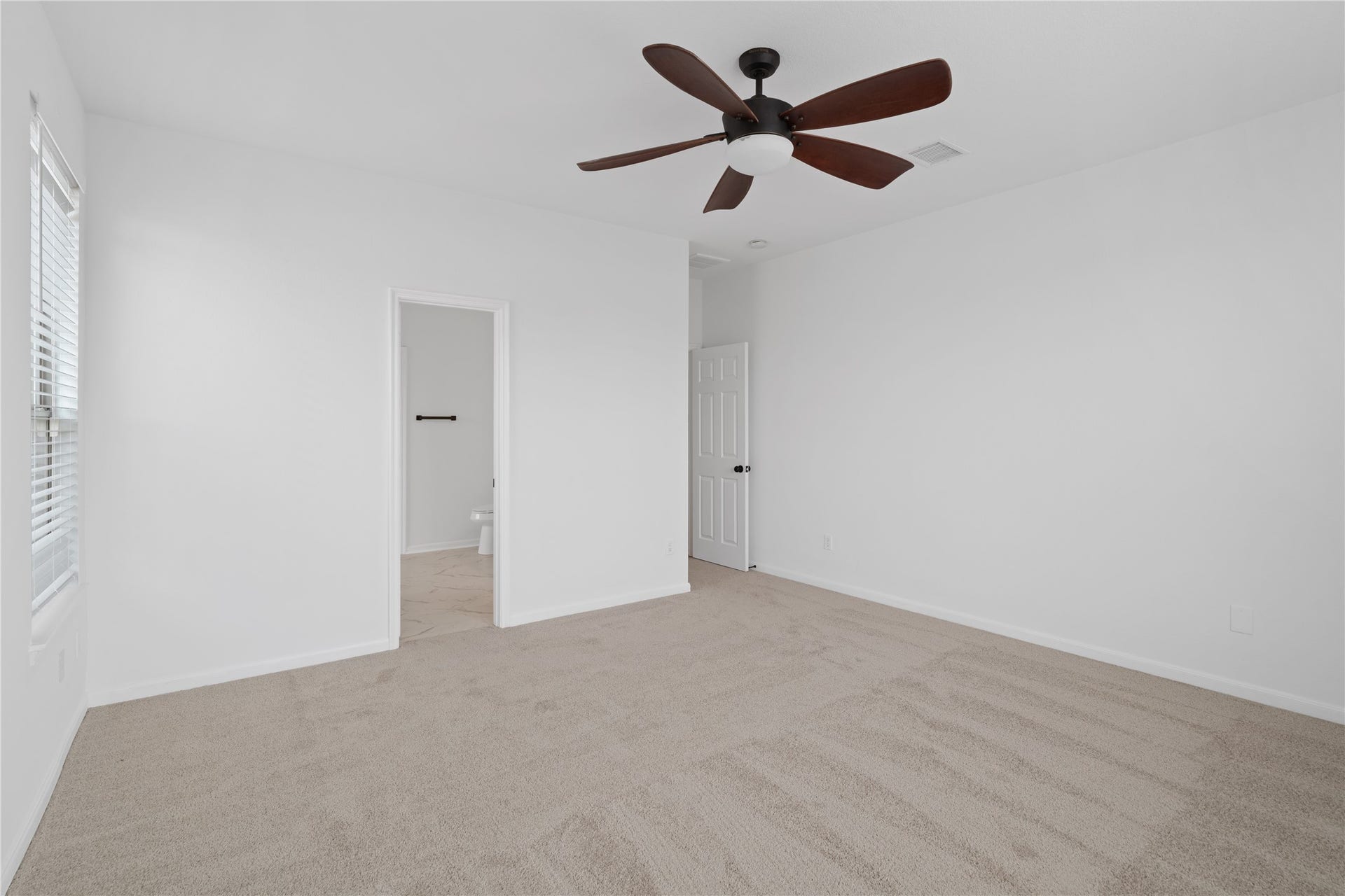 21611 Manitou Falls Lane, Katy, TX 77449 Primary Bedroom Generously proportioned primary bedroom featuring soft neutral carpet, a ceiling fan, and convenient access to the adjoining bathroom.