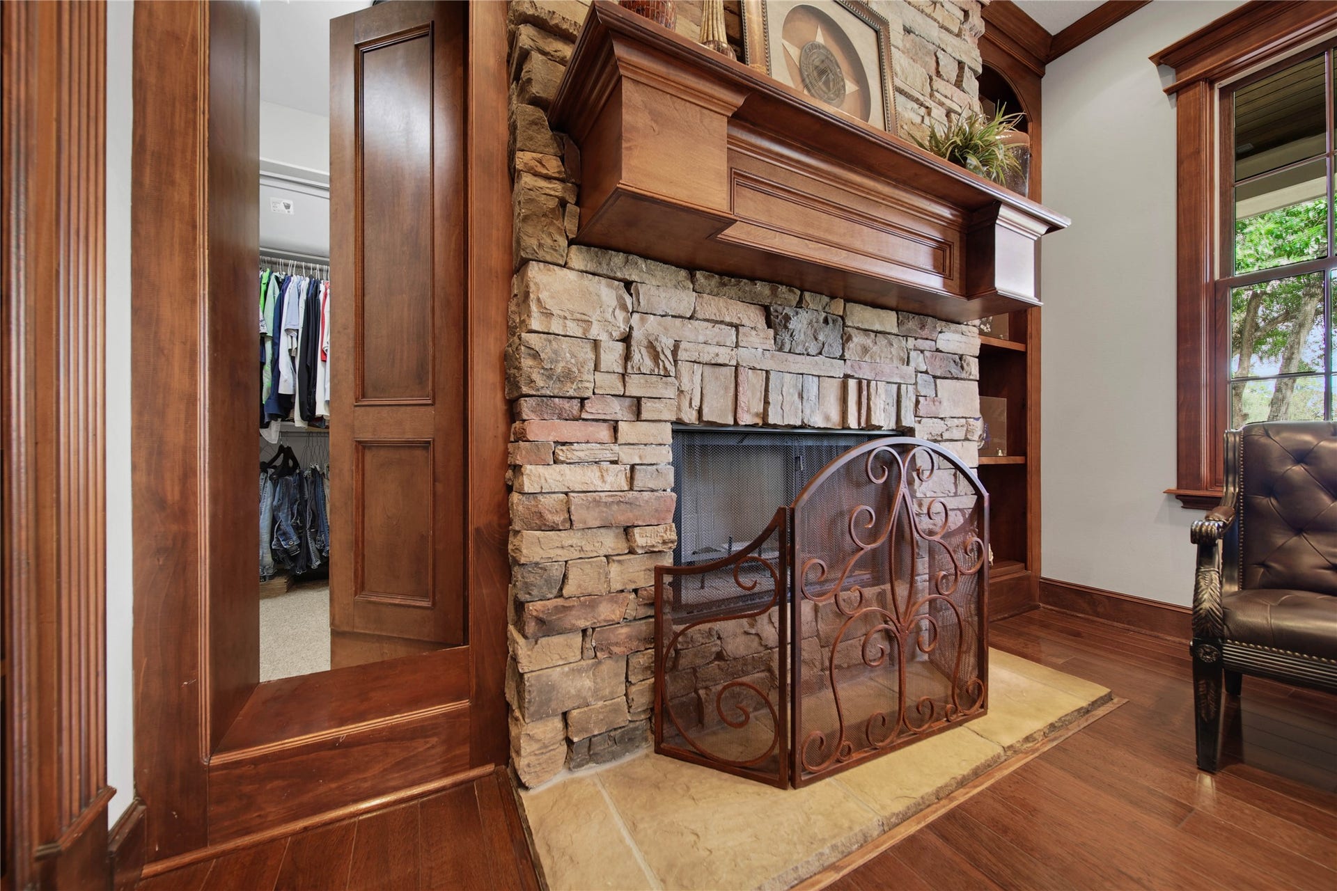 12635 Hunters Canyon Lane, Cypress, TX 77429 This space features a rustic stacked stone gas fireplace with a rich wood mantle, creating a cozy and inviting atmosphere, and complemented by hardwood floors. The small opening on the left is a secret door to one of the primary bedroom closets.