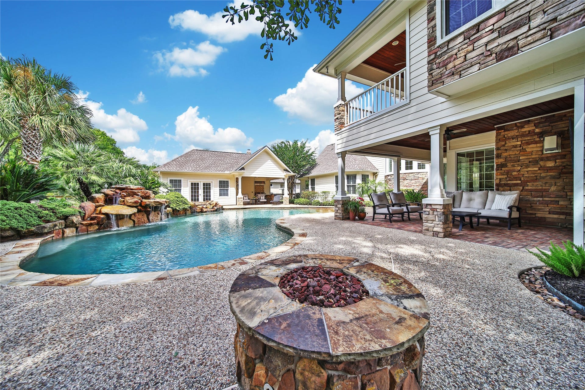 12635 Hunters Canyon Lane, Cypress, TX 77429 Experience luxury outdoor living with a stunning pool featuring a waterfall, surrounded by lush landscaping, a cozy fire pit, and ample patio seating under charming covered porches.