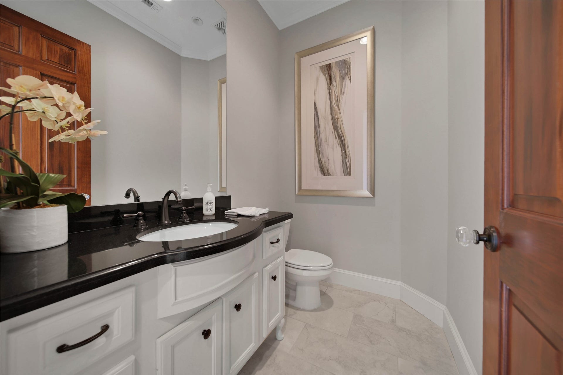 12635 Hunters Canyon Lane, Cypress, TX 77429 This elegant powder room featuring a sleek black granite countertop, white cabinetry, and modern fixtures, is located off the entry and the hallway leading to the private primary suite.