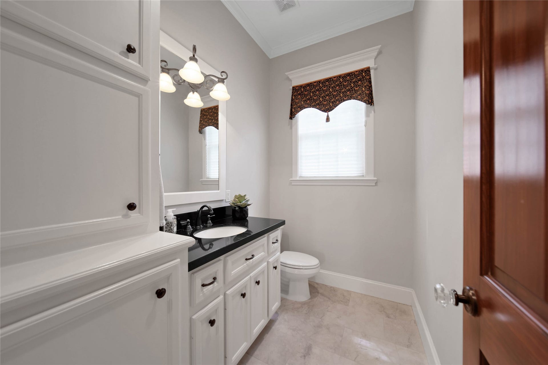 12635 Hunters Canyon Lane, Cypress, TX 77429 This charming half-bath located off the family room features classic white cabinetry, a sleek black countertop, and elegant light fixtures, complemented by a window with a decorative valance for natural light. There is a door that leads to the covered patio and can serve as a pool bath.