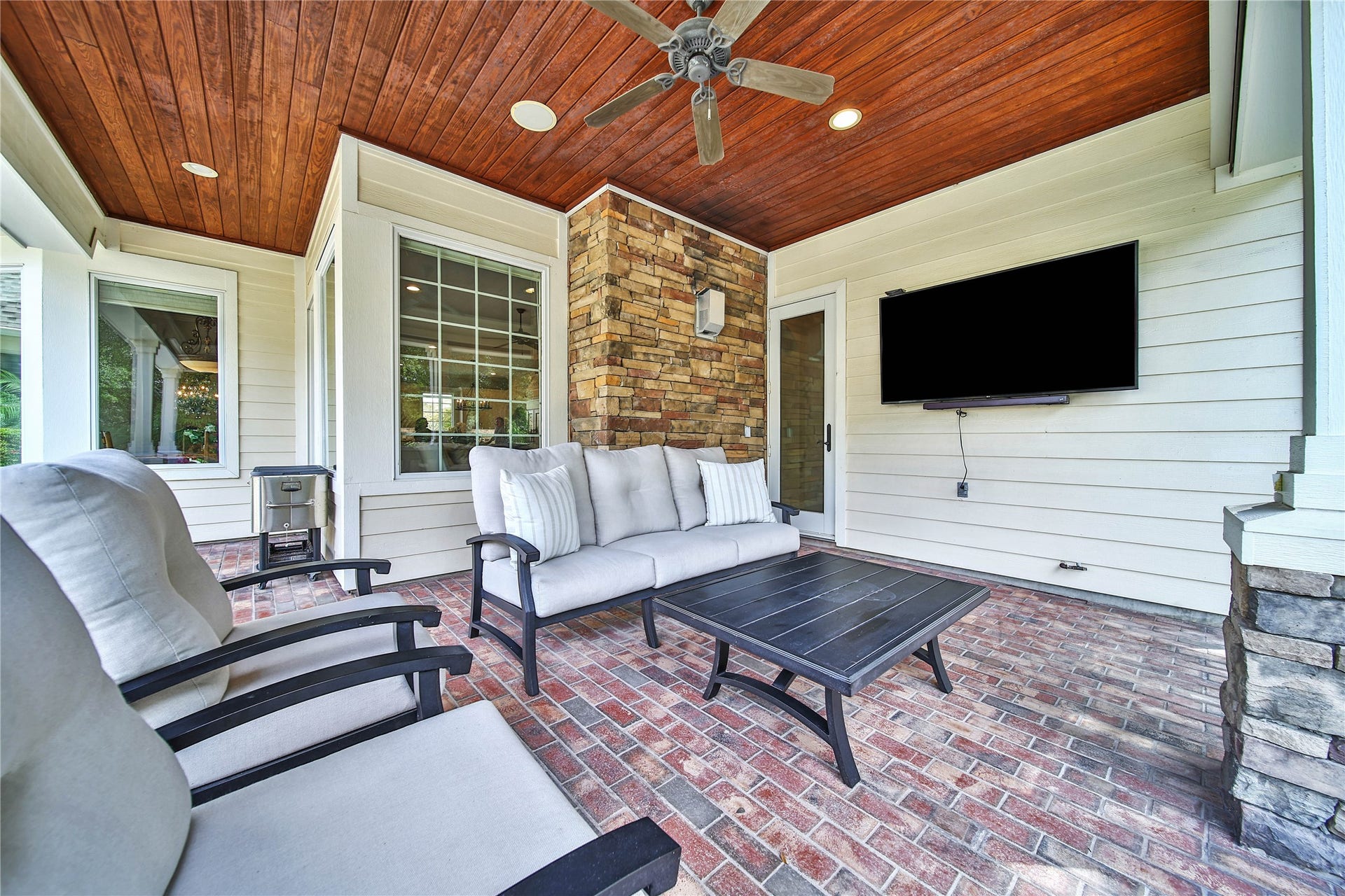 12635 Hunters Canyon Lane, Cypress, TX 77429 This is the main covered patio off the family room with brick flooring, tongue and groove ceilings, featuring a cozy seating area, stacked stone accent wall, perfect for outdoor entertainment. There are surround sound speakers outside, as well.