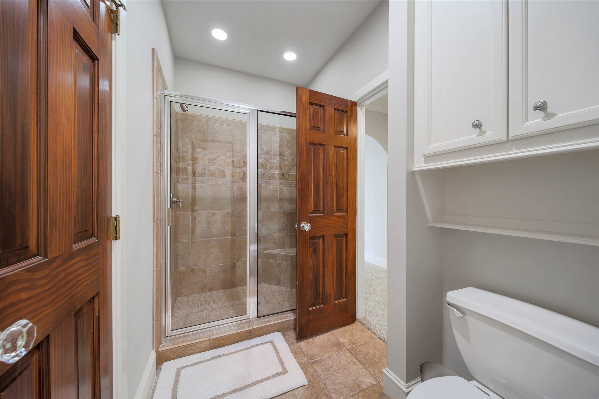 12635 Hunters Canyon Lane, Cypress, TX 77429 Elegant bathroom featuring a tiled walk-in shower, rich wooden door, and ample cabinetry for storage.