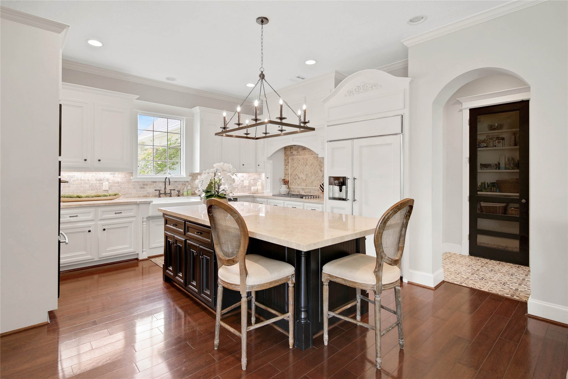 12635 Hunters Canyon Lane, Cypress, TX 77429 The spacious island with seating, sleek countertops, and a stylish chandelier is the perfect spot for an informal meal. Custom cabinetry, hardwood floors, and a charming pantry door add to its appeal.