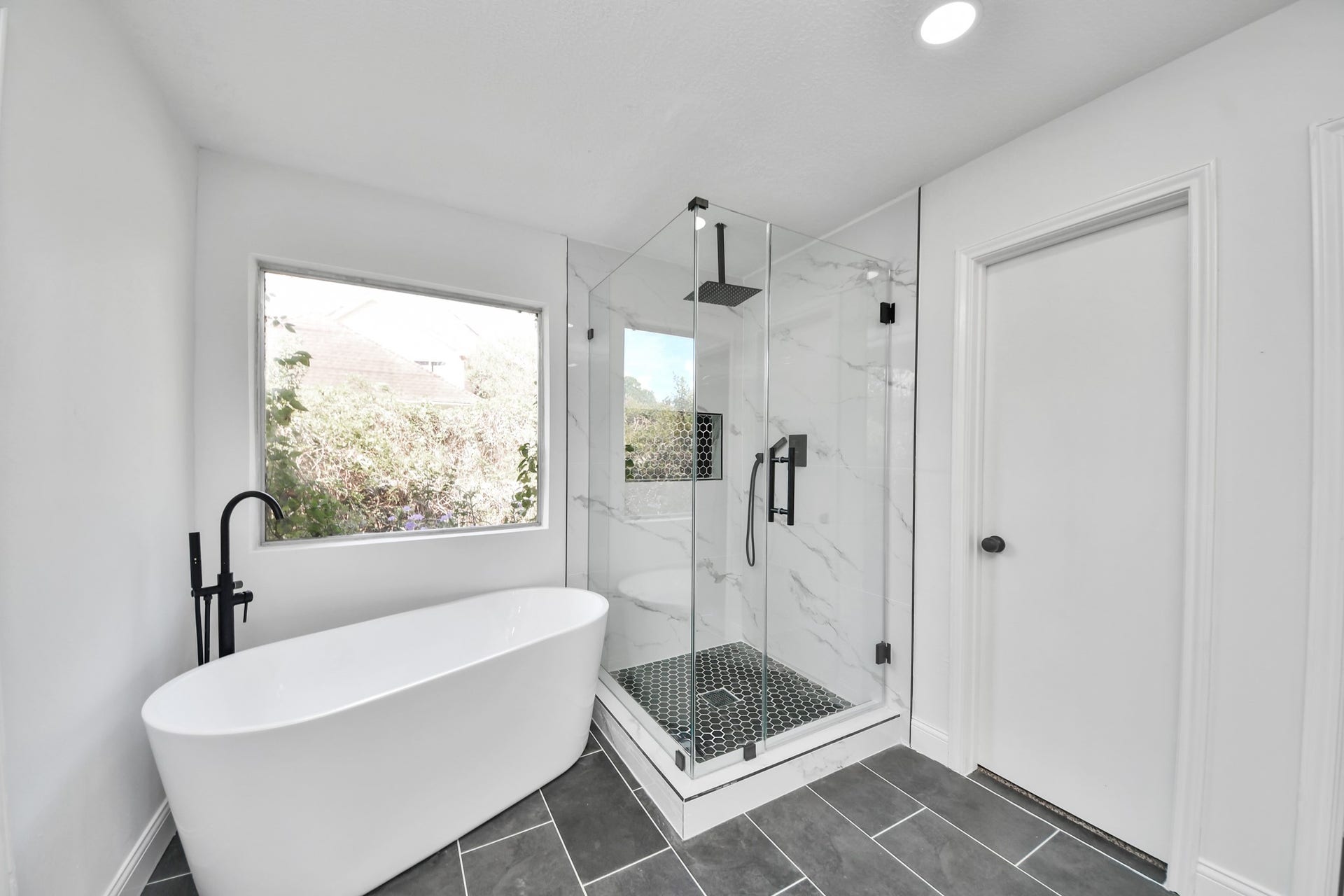 8503 Rebawood Drive, Humble, TX 77346 Luxurious bathroom featuring a sleek freestanding tub, a modern glass-enclosed shower with elegant tilework, and abundant natural light through a large window.