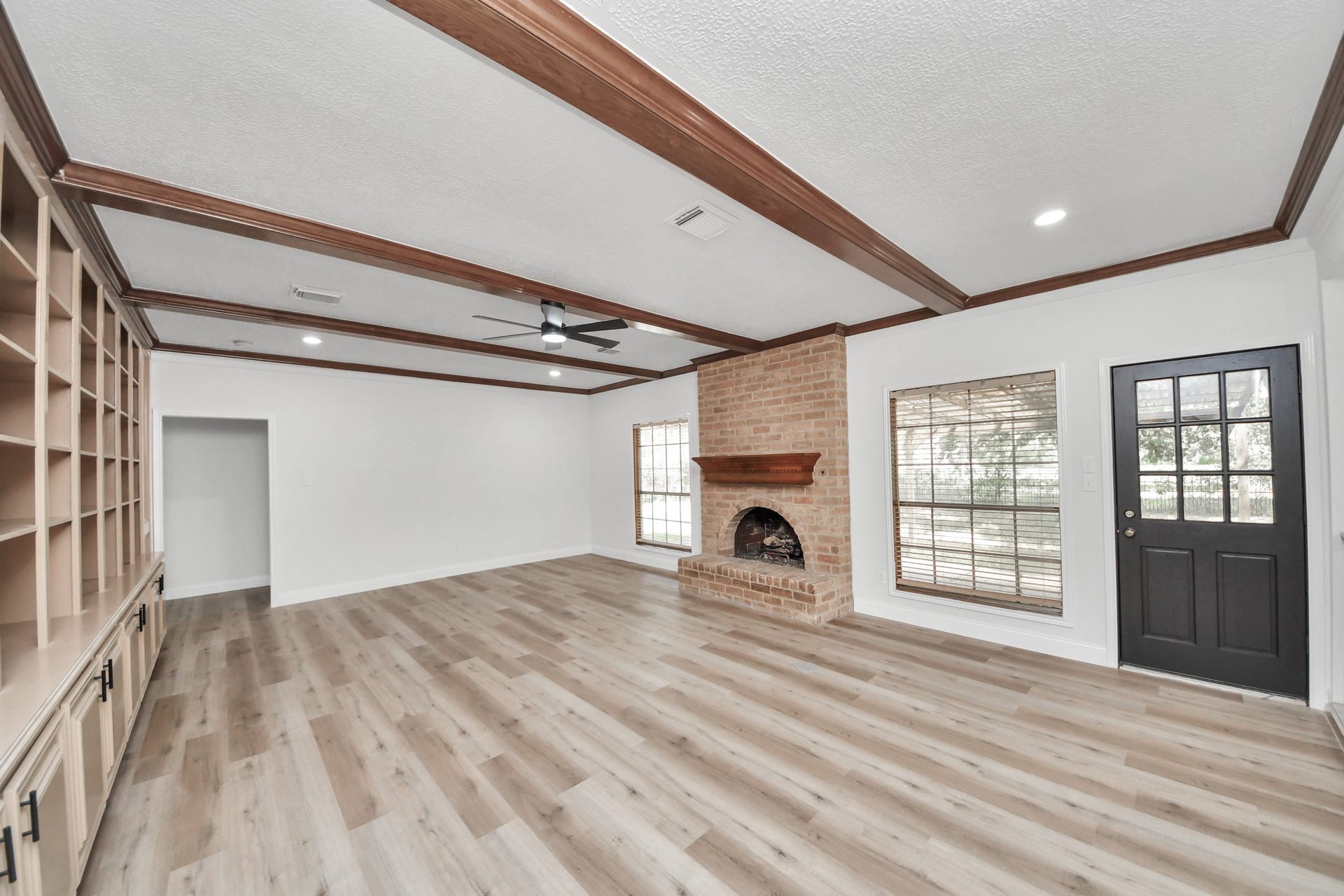 8503 Rebawood Drive, Humble, TX 77346 Spacious living room featuring elegant wood-beamed ceilings, a cozy brick fireplace, built-in shelving, and abundant natural light.