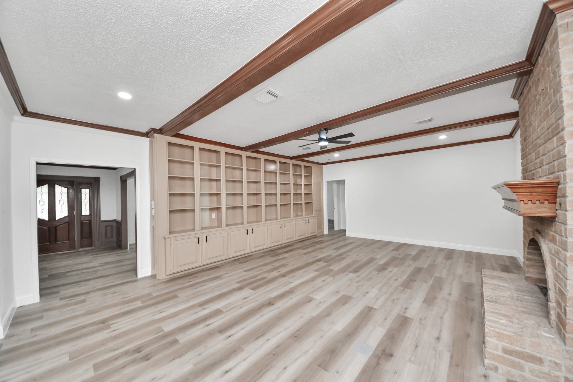 8503 Rebawood Drive, Humble, TX 77346 Spacious living room with elegant built-in shelving, a cozy brick fireplace, and rich wooden ceiling beams, perfect for relaxation and entertaining.