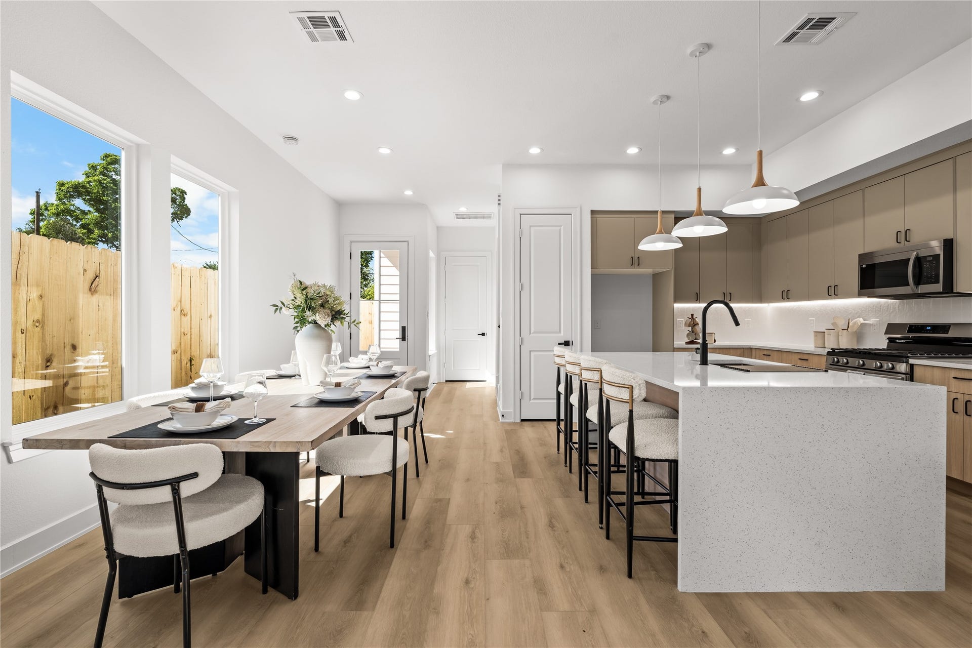 The main floor layout keeps everything open and connected. Light flooring and white walls maximize the natural light throughout the entire space. From the dining area, you have a direct view of the kitchen, which features a breakfast bar with seating and modern pendant lighting.