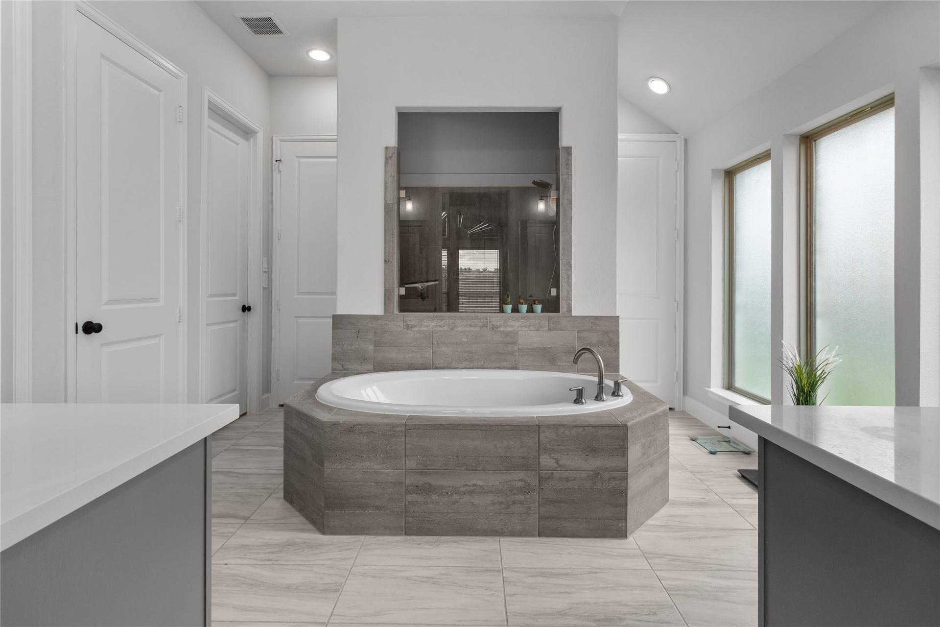30427 Watershed Way, Fulshear, TX 77441 This bathroom features a central oval bathtub with a stylish tile surround. It has a modern, sleek design with ample natural light from large frosted windows, creating a serene and private atmosphere.