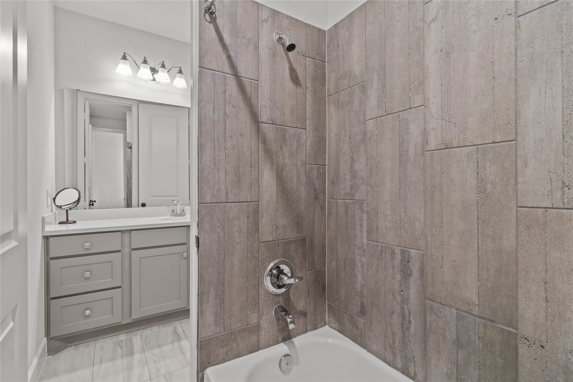 30427 Watershed Way, Fulshear, TX 77441 Bathroom features a modern design with large, neutral-toned tiles in the shower and a sleek vanity with ample storage. The lighting above the mirror adds brightness, creating a clean and inviting space.