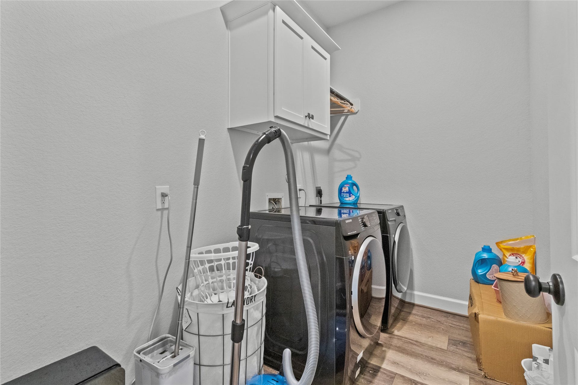 30427 Watershed Way, Fulshear, TX 77441 A functional laundry room featuring modern washer and dryer units, overhead storage cabinets, and ample space for cleaning supplies and laundry essentials.