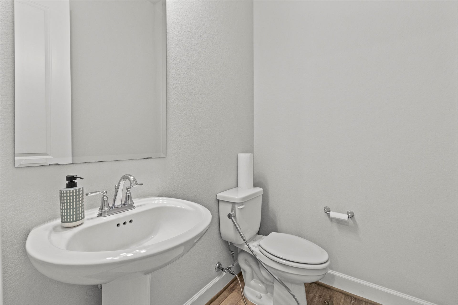 30427 Watershed Way, Fulshear, TX 77441 This is a compact, modern half-bathroom featuring a pedestal sink, a toilet, and a wall-mounted mirror, with neutral-colored walls and flooring.