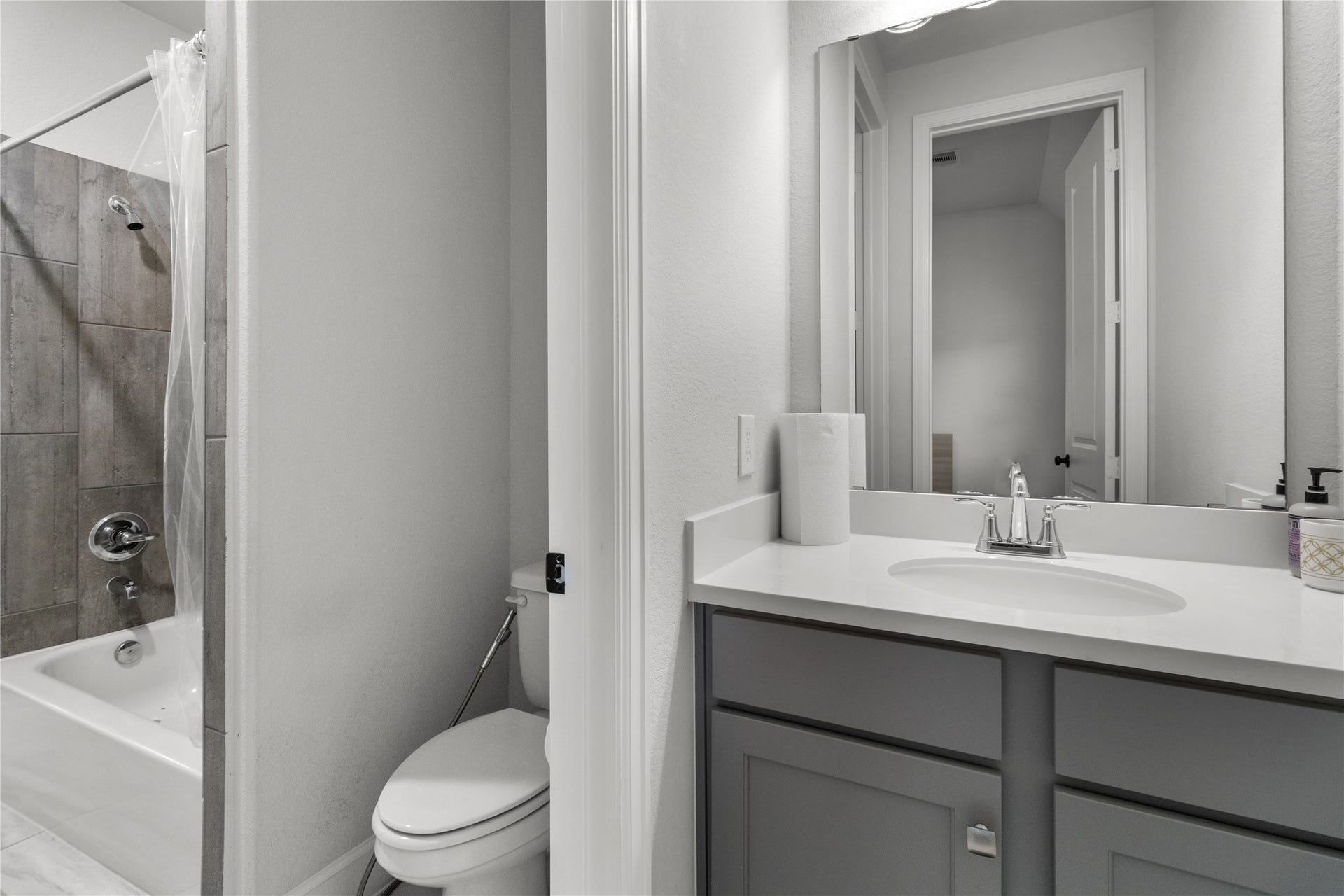 30427 Watershed Way, Fulshear, TX 77441 Modern bathroom featuring a sleek vanity with a large mirror, a toilet, and a bathtub with a tile backsplash. The space is bright and well-lit.