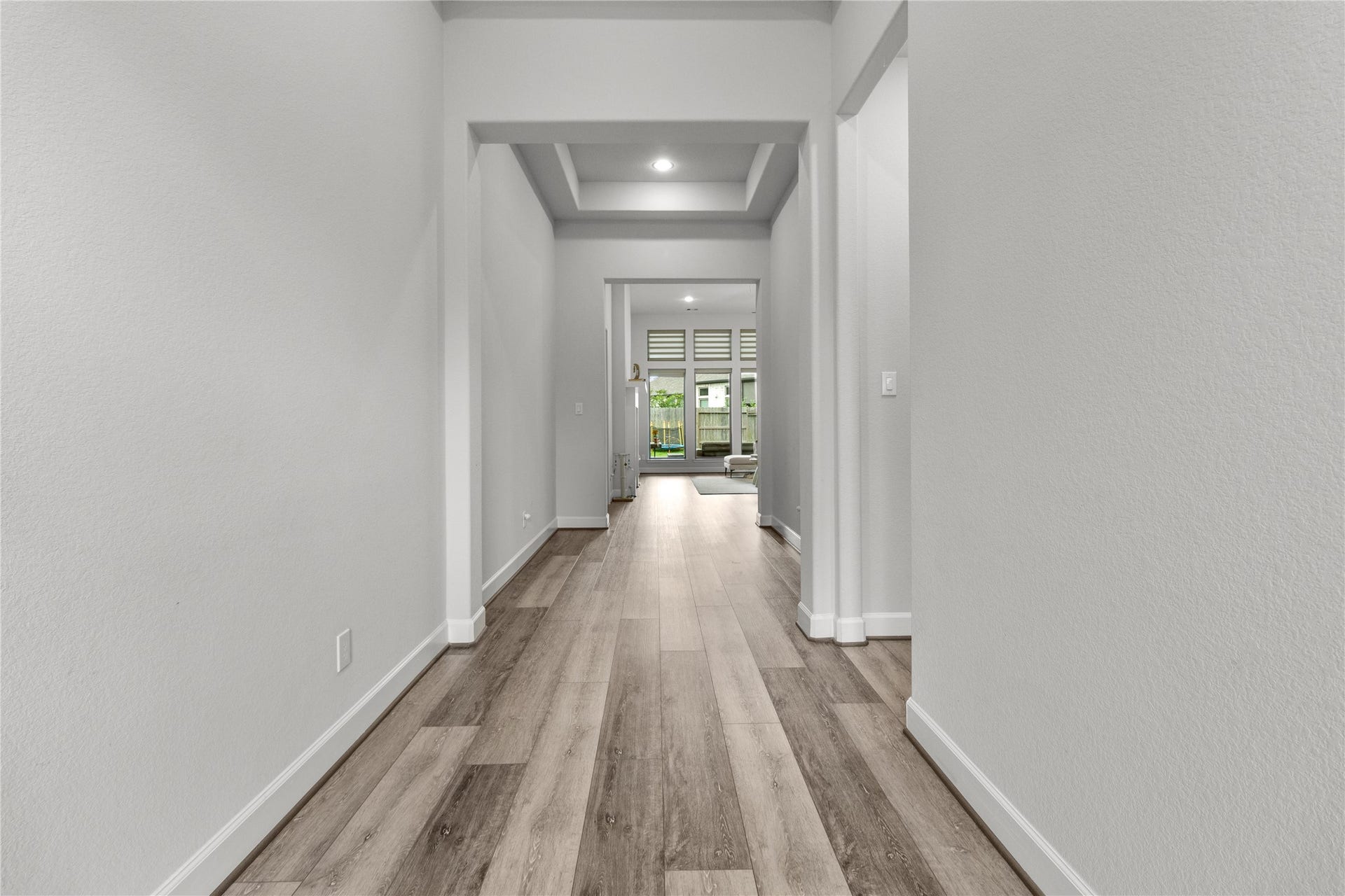 30427 Watershed Way, Fulshear, TX 77441 Modern, well-lit hallway with light wood flooring and neutral walls, leading to a bright living area with large windows.