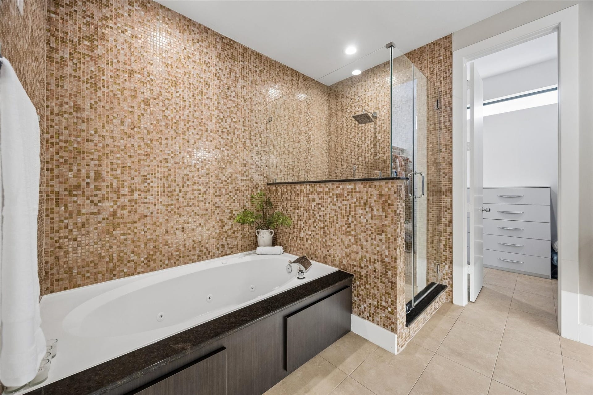 The primary bath brings a spa-like feel to everyday routines with a jetted soaking tub, glass-enclosed shower, warm mosaic tile, and sleek modern finishes. Direct access to the custom walk-in closet keeps mornings easy, while the polished design makes the whole space feel calm and relaxing.
