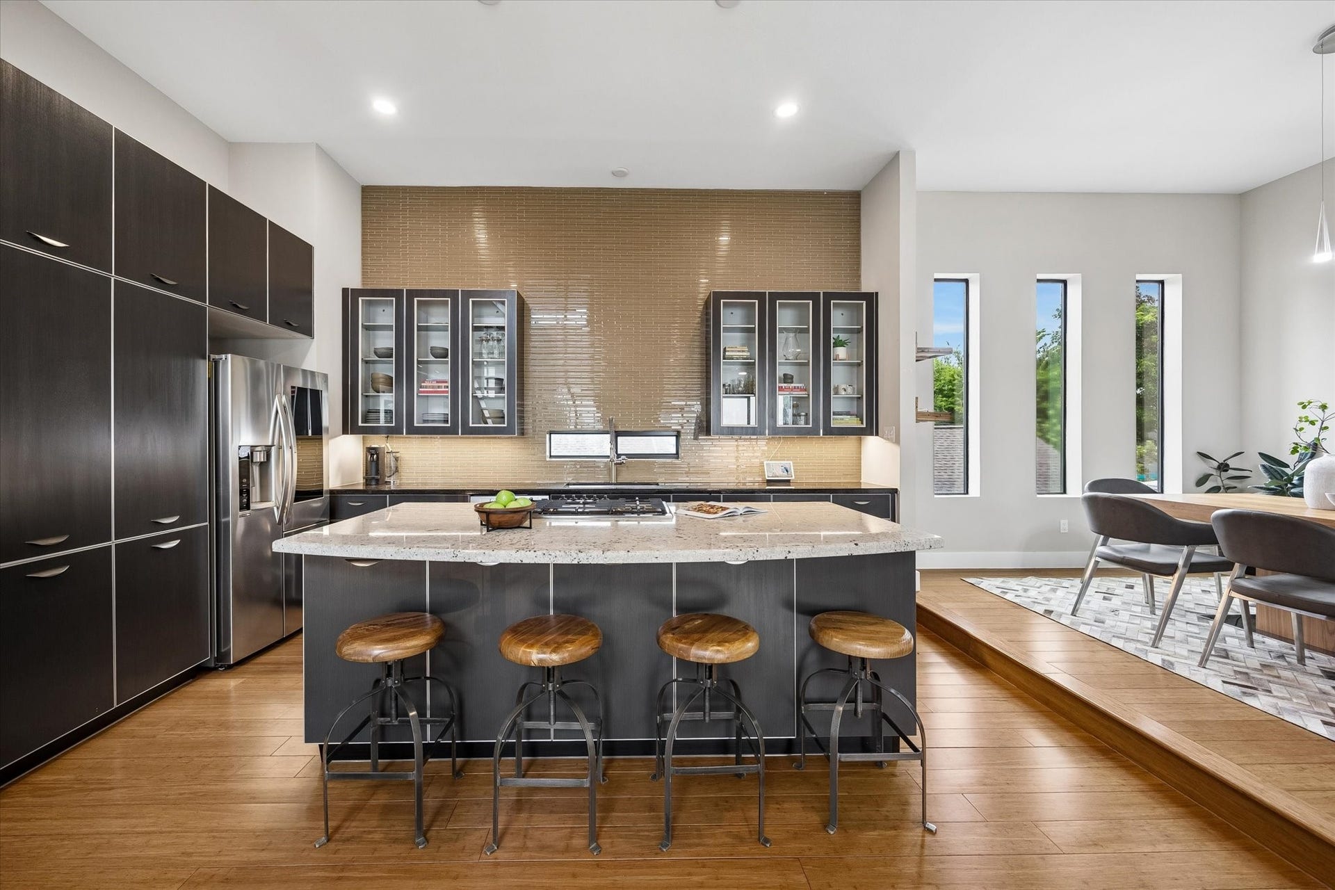 The kitchen offers a clean contemporary feel with extensive cabinetry, sleek stainless-steel appliances, under-cabinet lighting, and a striking tiled wall that adds warmth and texture. Bar seating at the island offers the perfect perch to visit with the chef while dinner comes together.